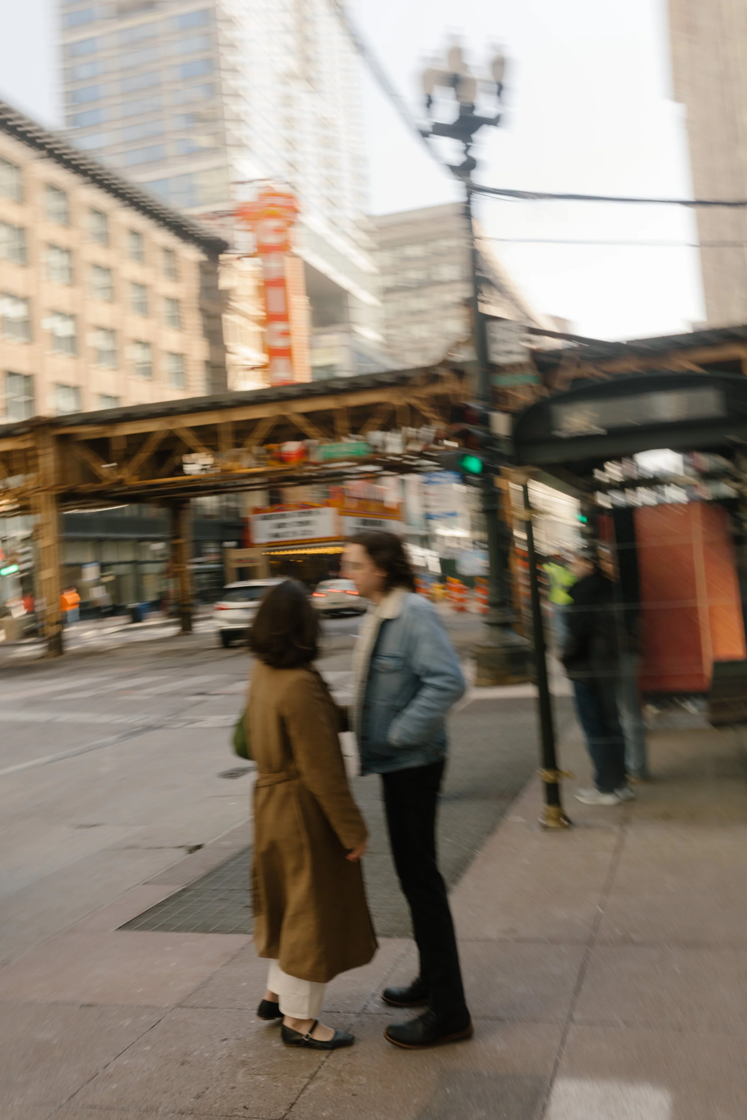 Candid street photo of couple pausing on a city sidewalk near a bus stop with urban movement around them