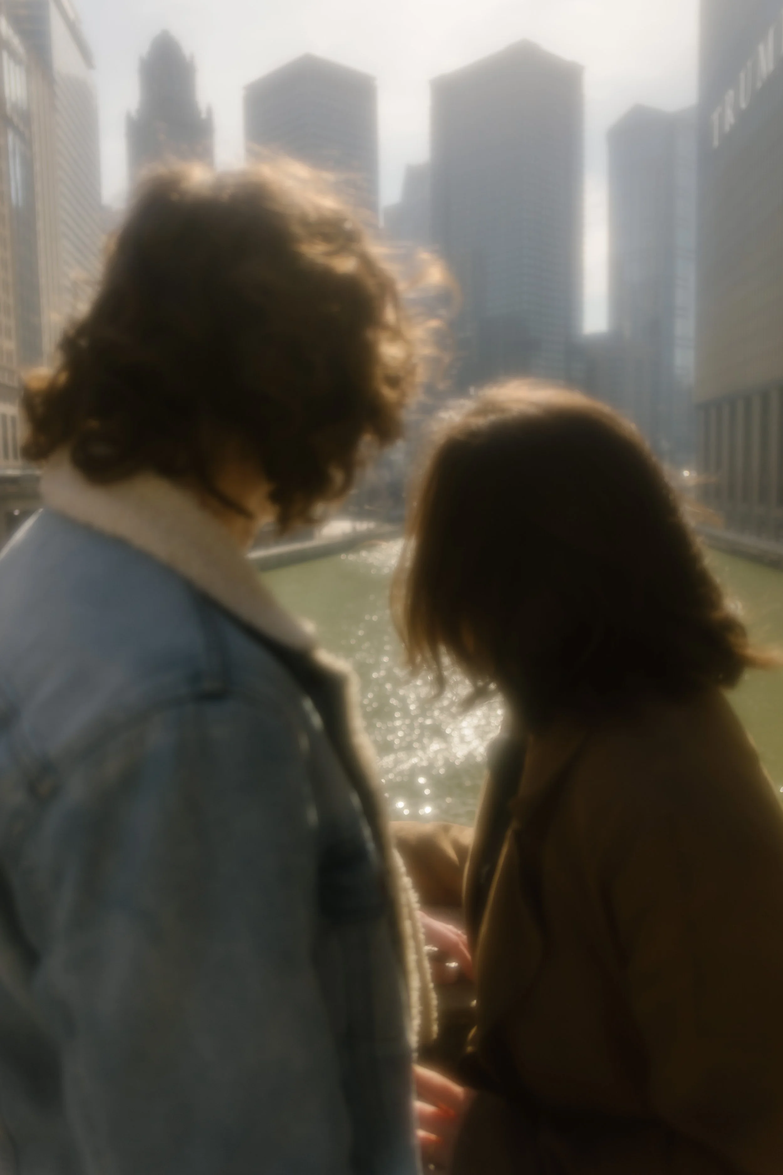 Soft, slightly blurred image of couple standing by the river with sunlight reflecting off the water and skyline behind them