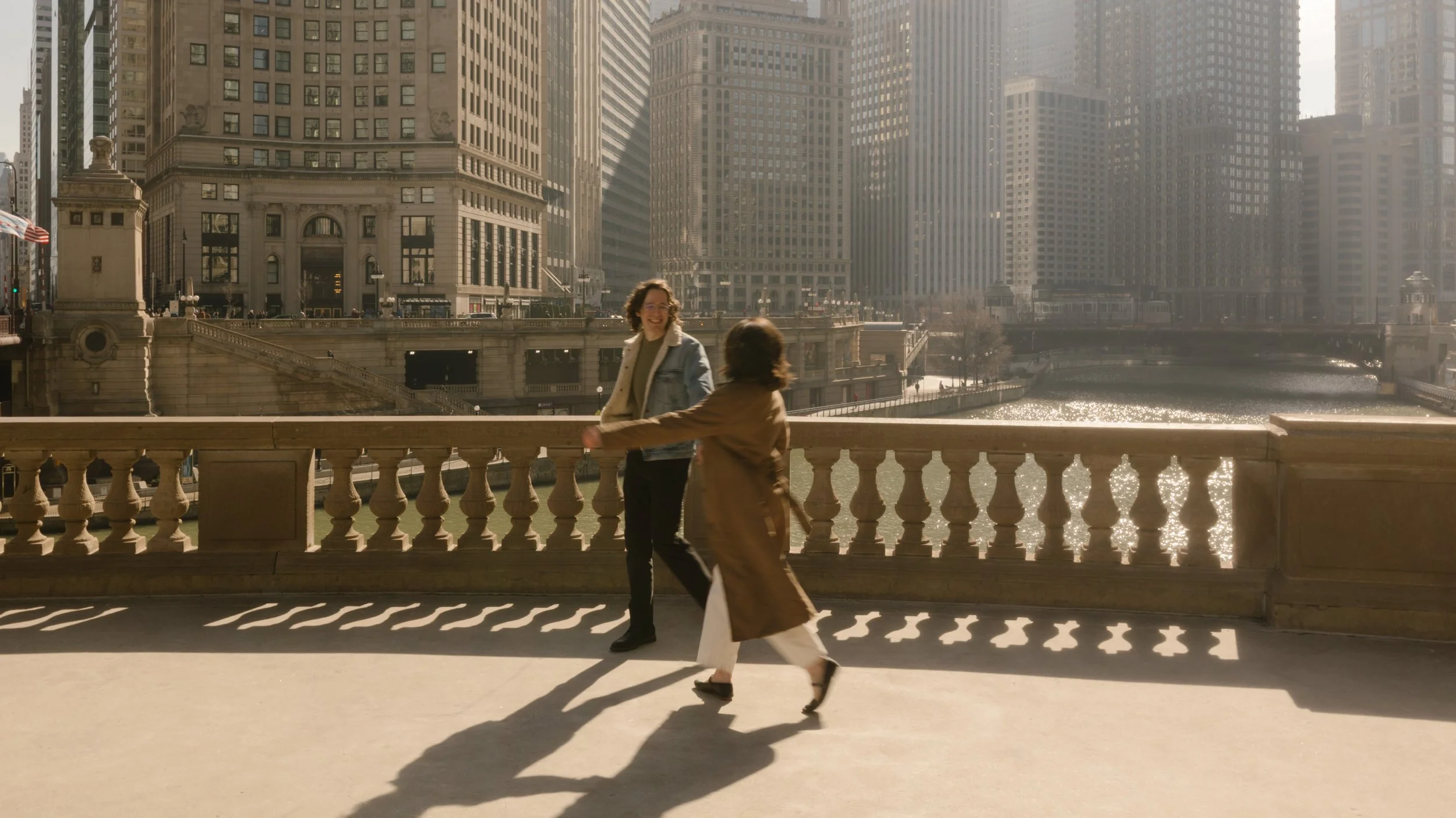 Couple running and spinning on a bridge overlooking downtown during engagement photos in Chicago with long shadows and afternoon light