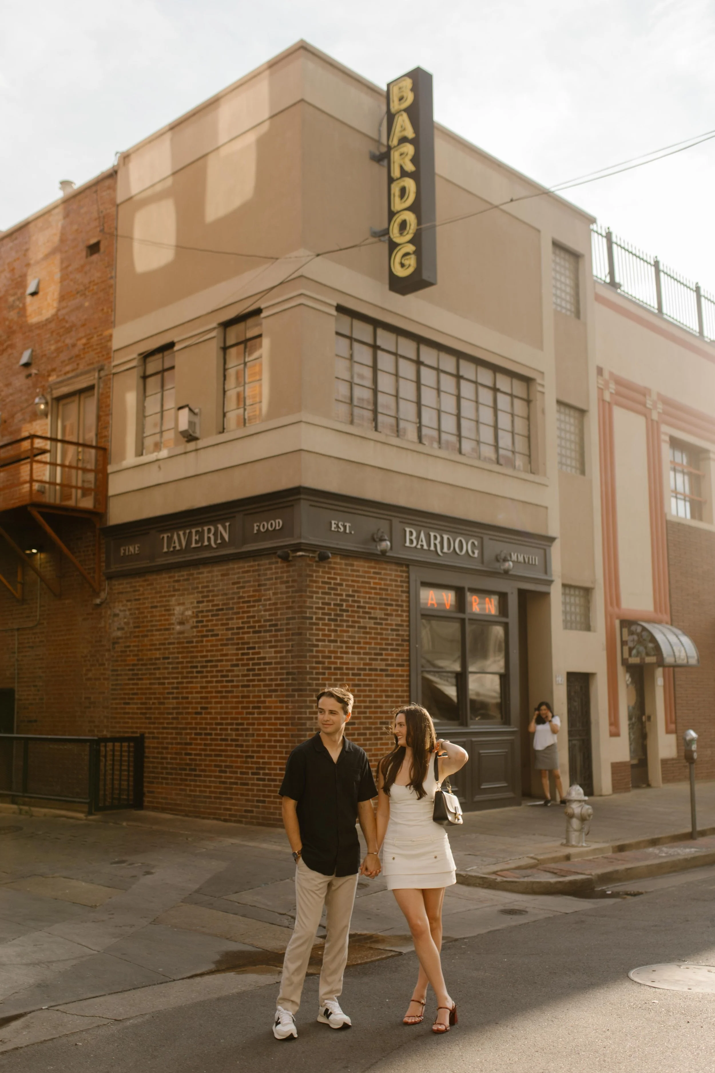 Couple standing at a street corner near a restaurant with warm evening light during new york city engagement photos