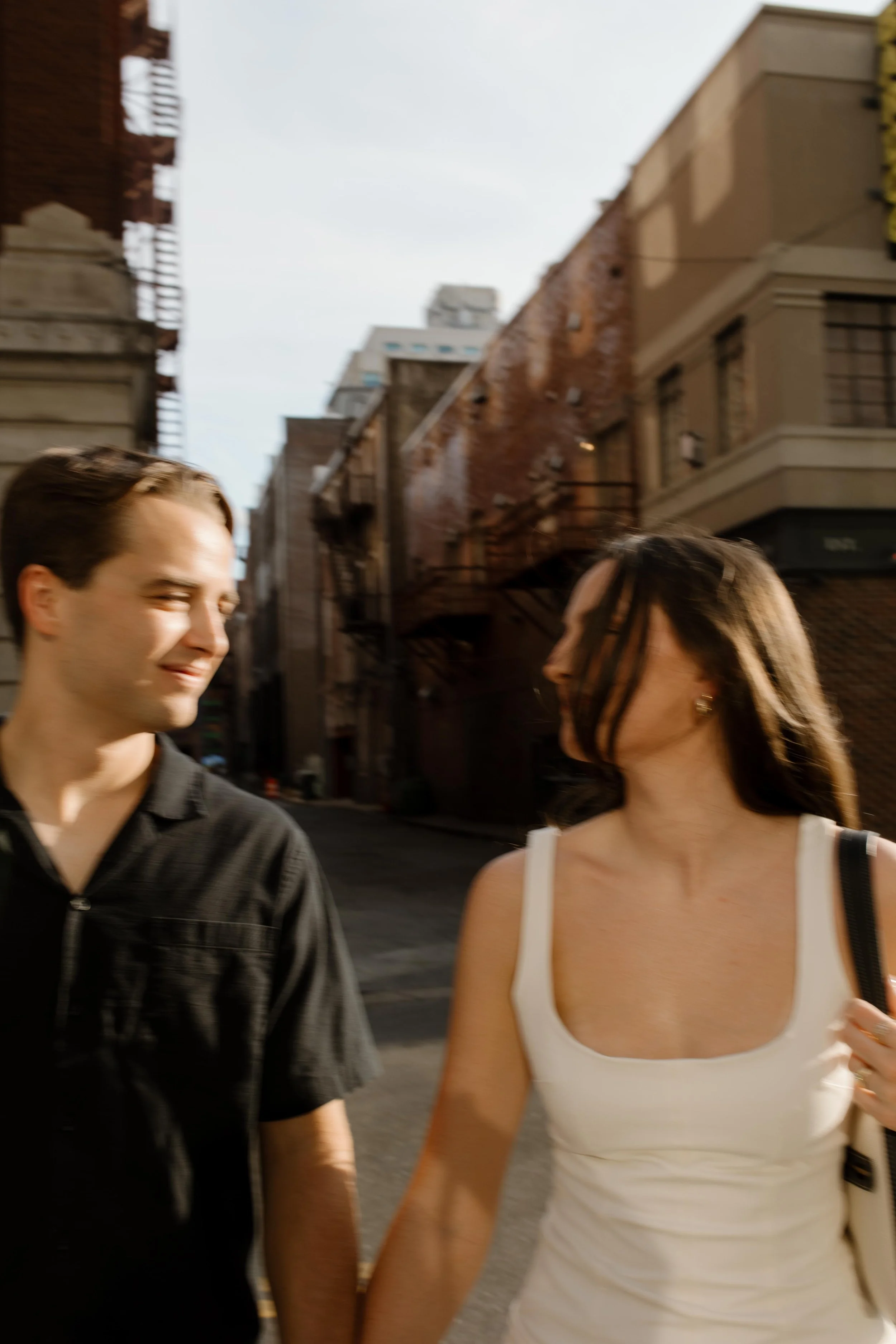 Close up of couple walking side by side looking at each other with soft golden hour lighting in a city setting