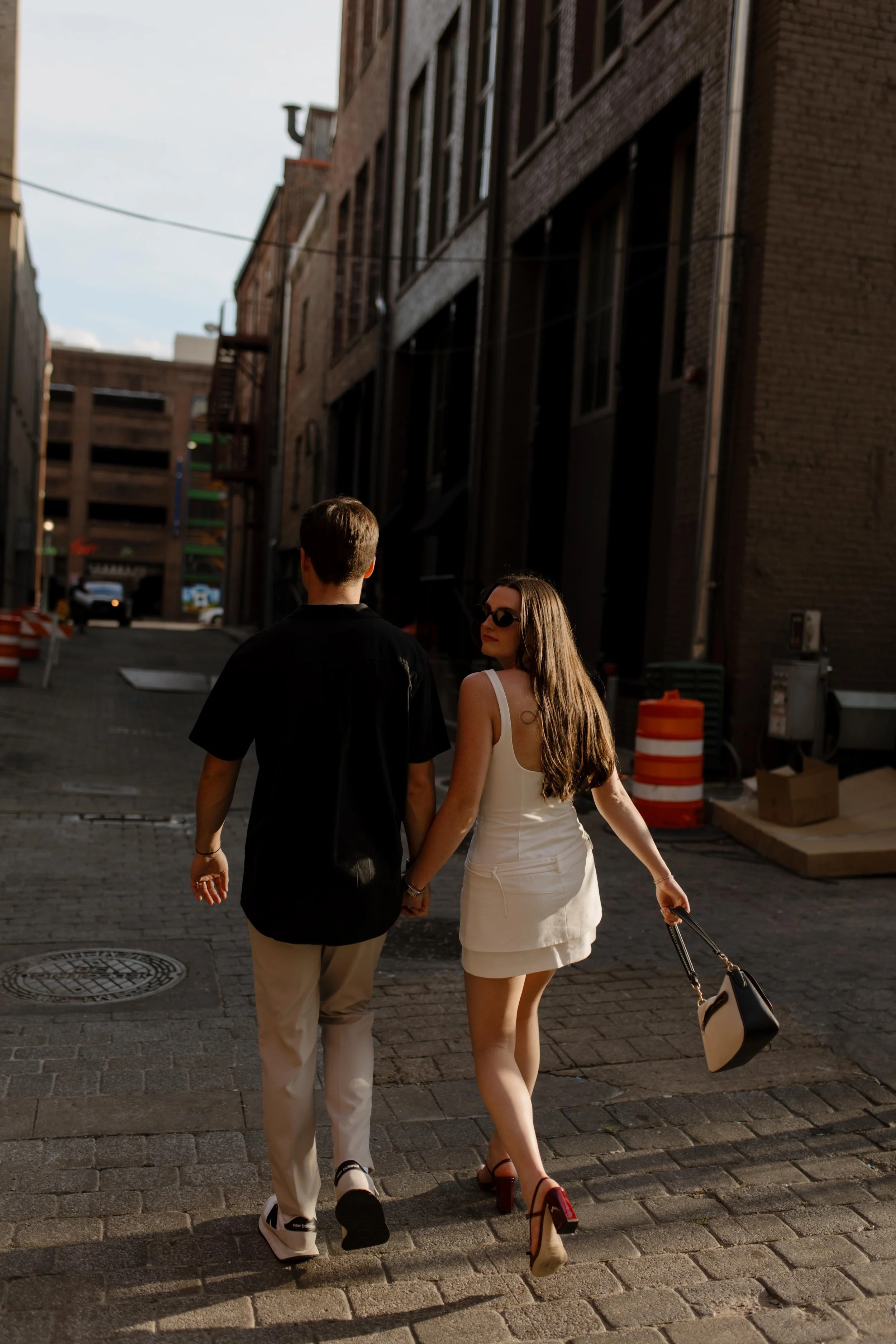 Couple walking away down a quiet city street holding hands with long shadows and evening light during new york city engagement photos
