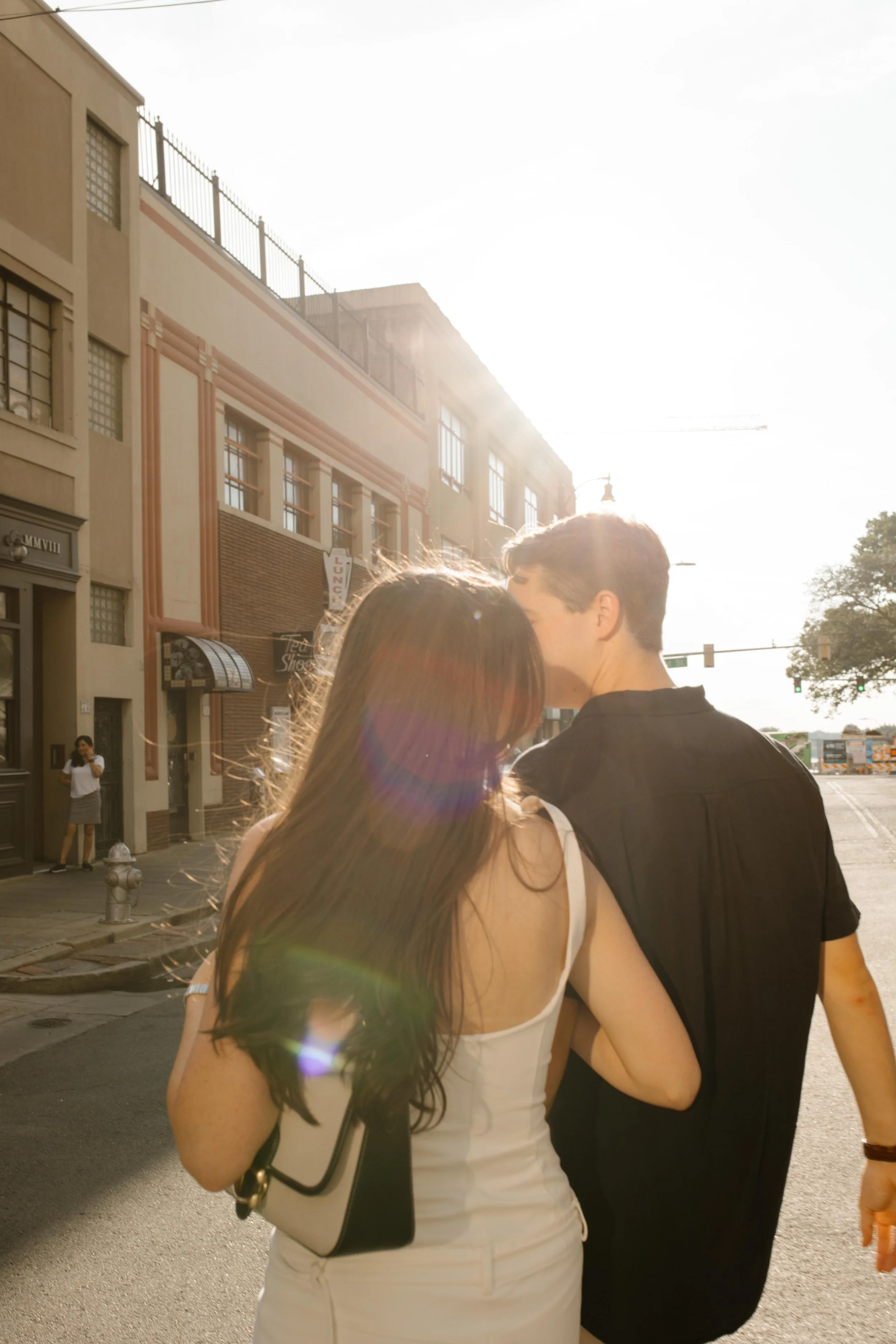 Couple walking into golden hour light with sun flare in a downtown setting during new york city engagement photos