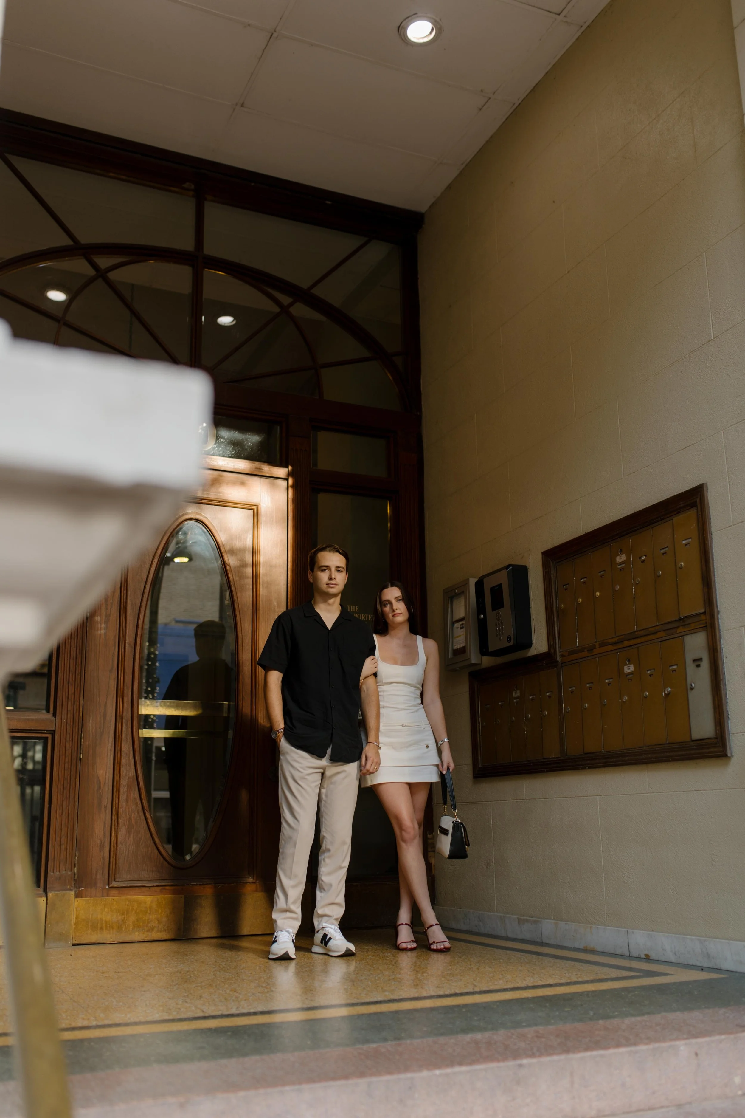 Couple standing together in a building entryway with warm tones and an editorial engagement session feel