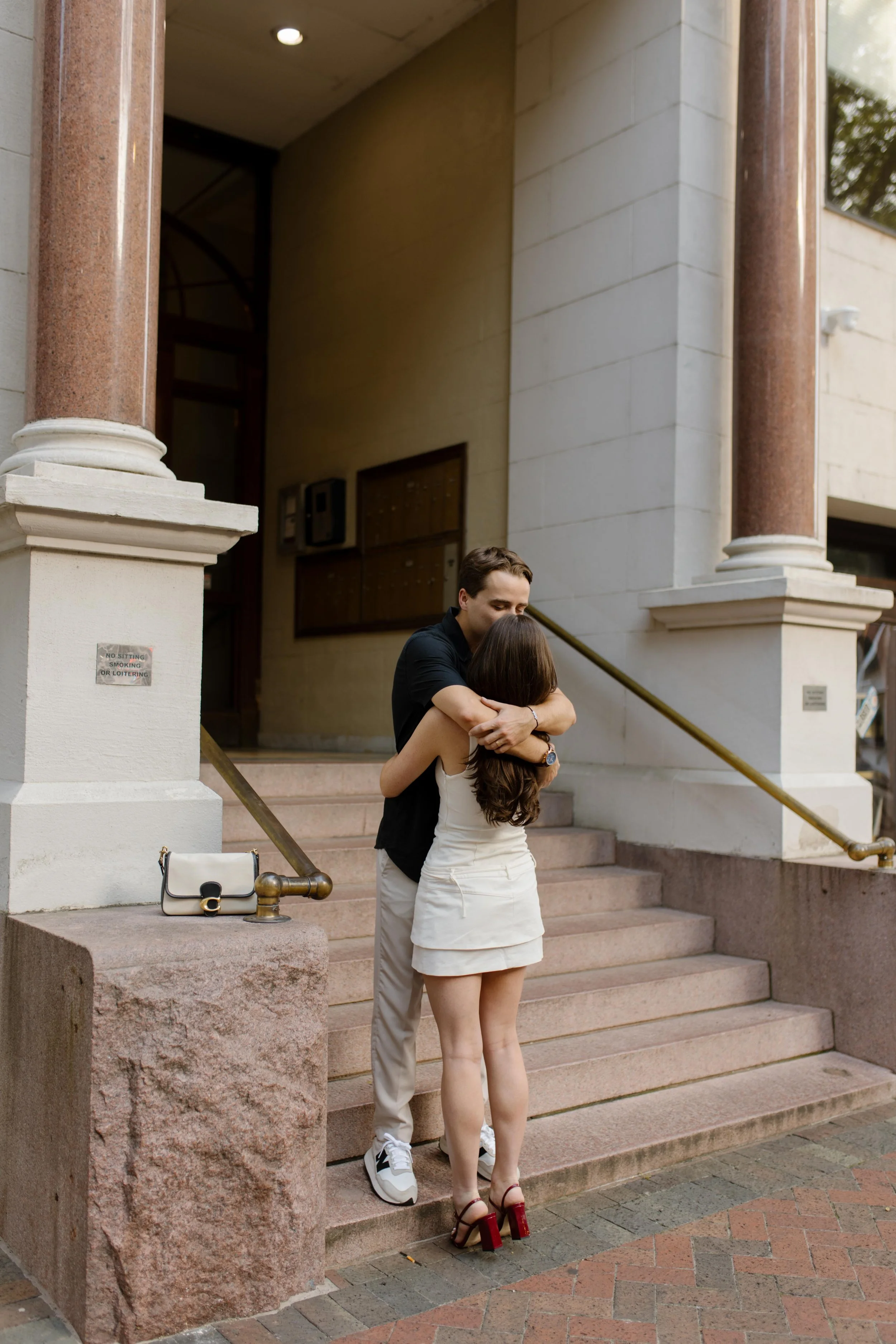 Couple embracing on stone steps outside a historic building during new york city engagement photos with a quiet, intimate feel