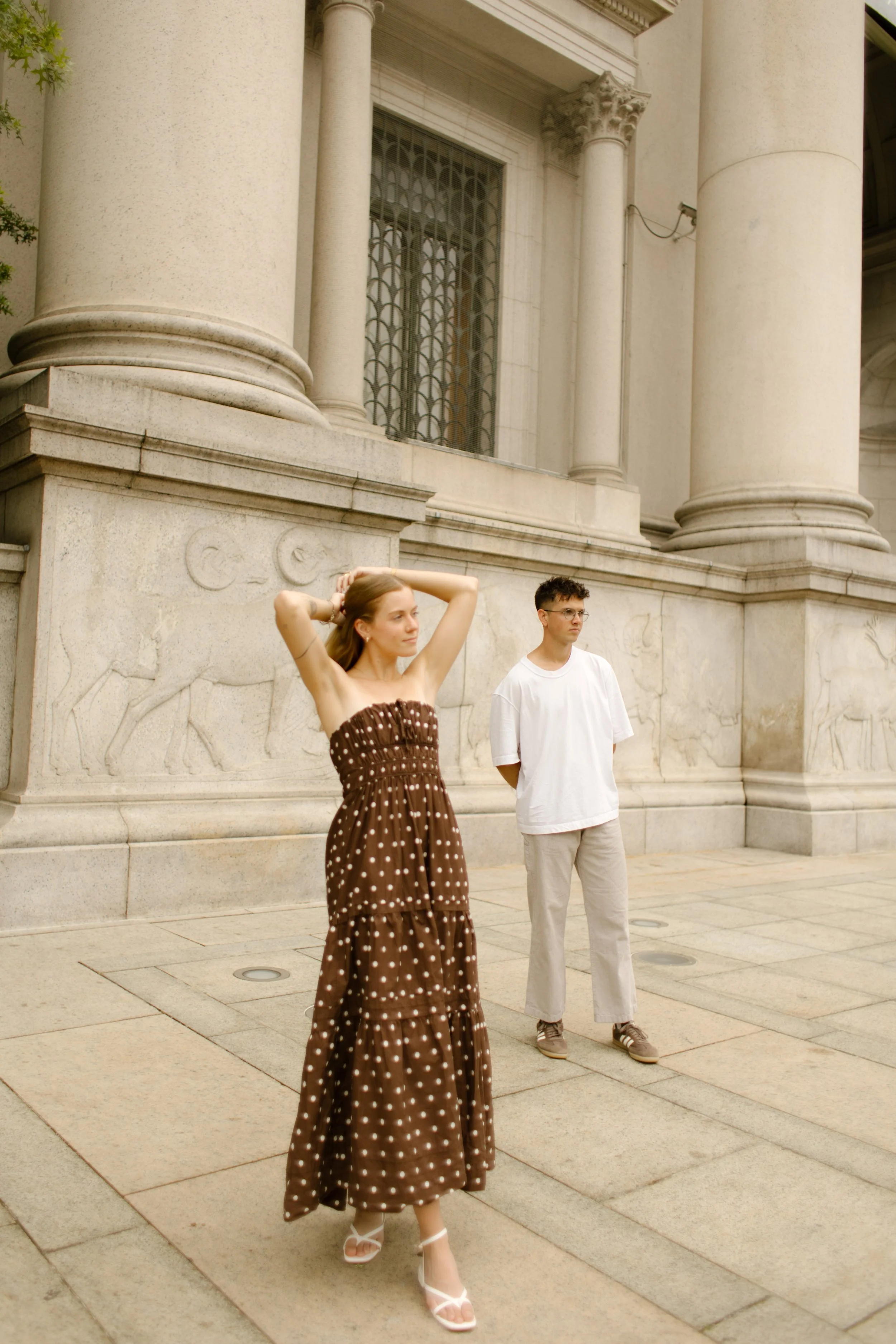 Couple walking past grand stone columns at a historic New York building, relaxed and in motion