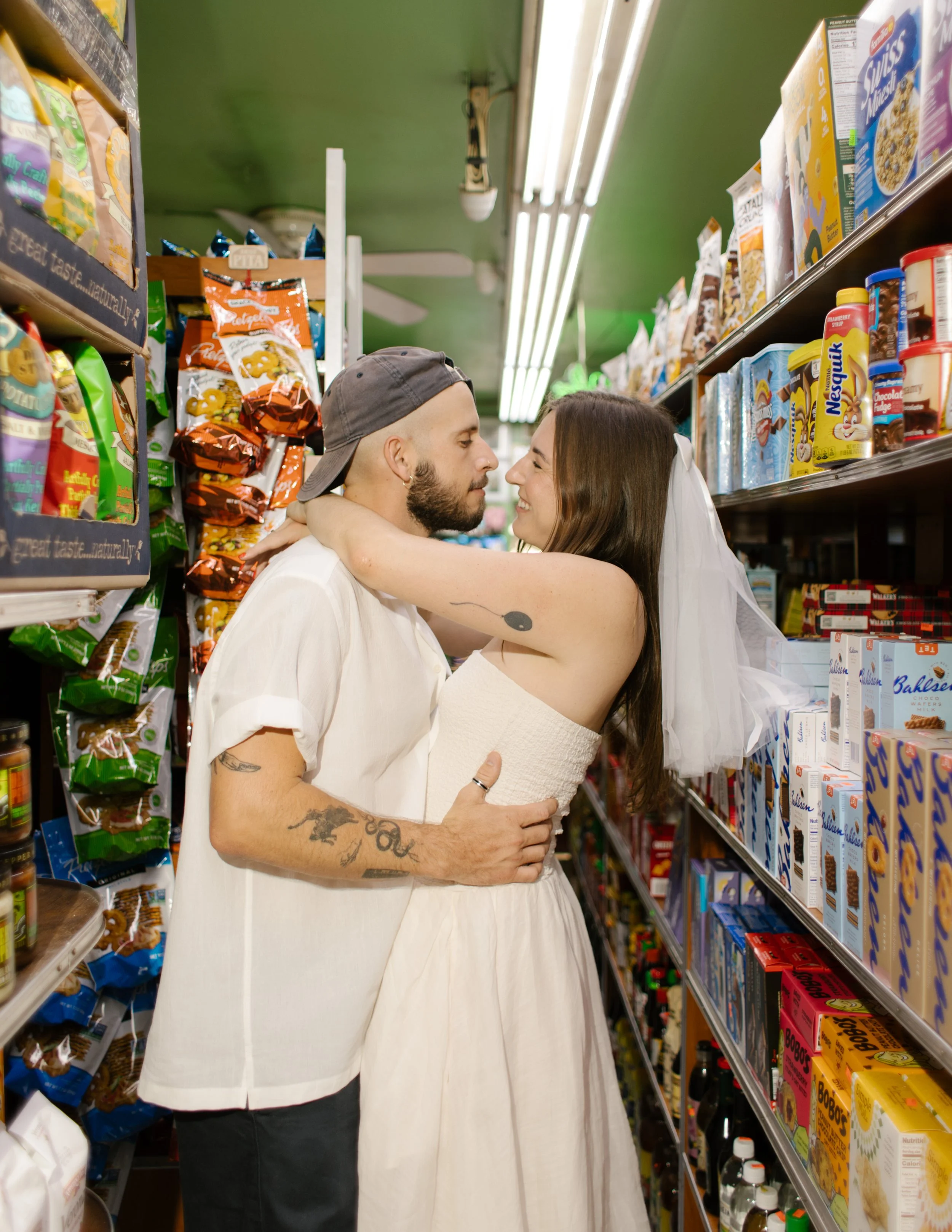 Playful couple embracing in a corner grocery store aisle, candid and close — New York engagement photographer perspective