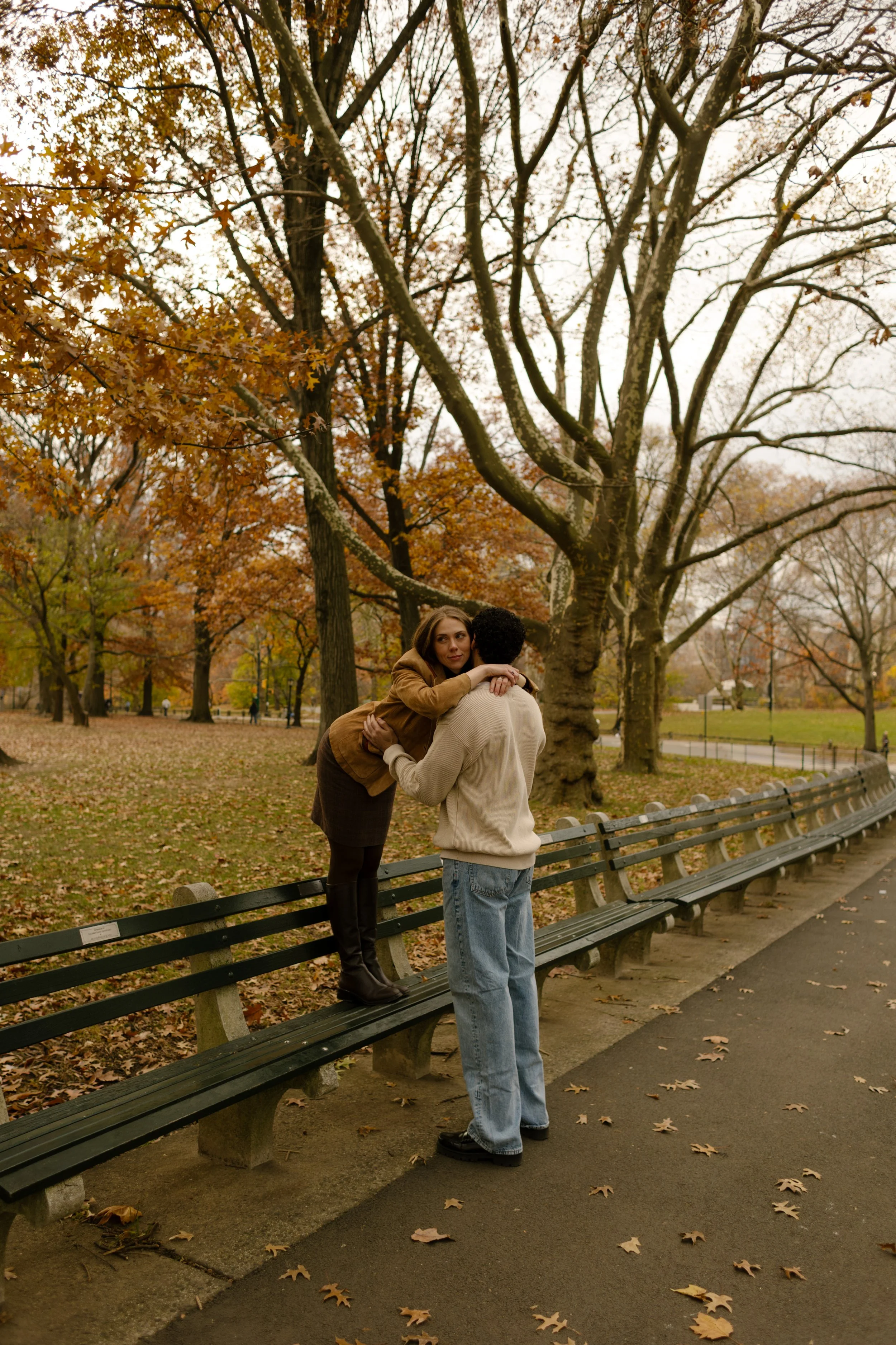 Couple embracing on a Central Park bench surrounded by fall foliage — photographed by a New York engagement photographer
