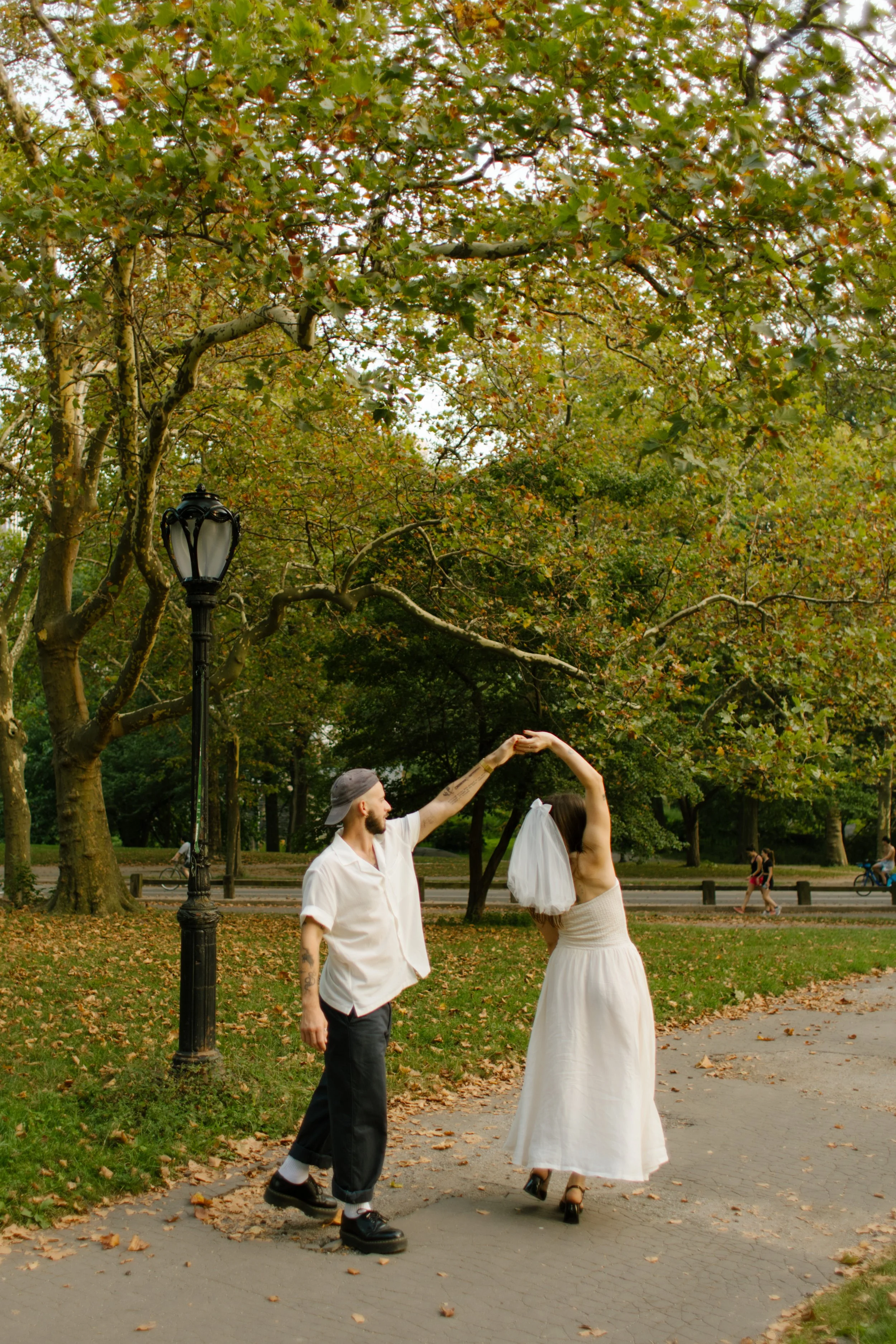 Couple spinning together on a tree-lined Central Park path, playful and unposed