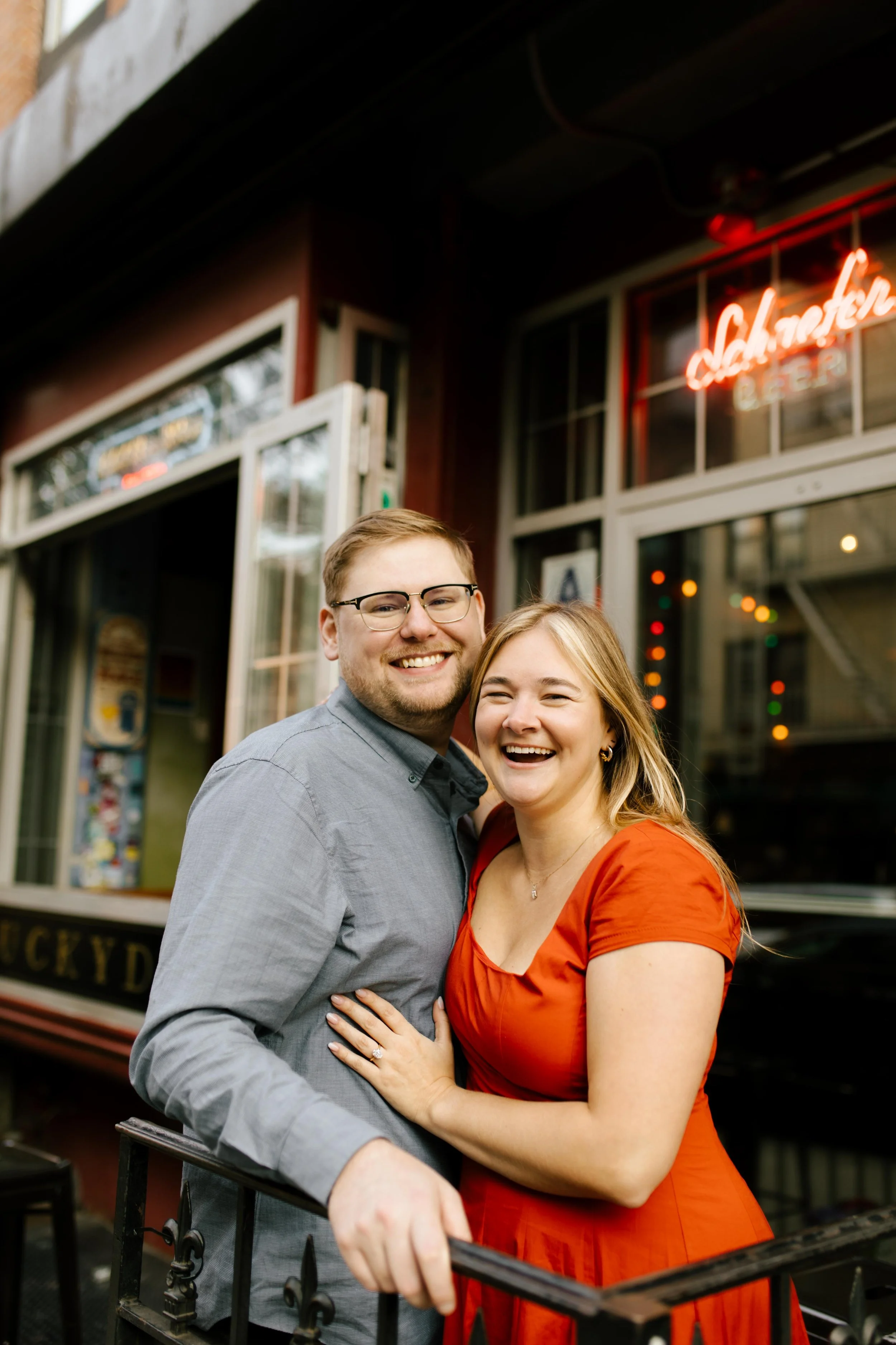 Smiling couple posing outside a neighborhood bar during their candid Brooklyn engagement photoshoot.