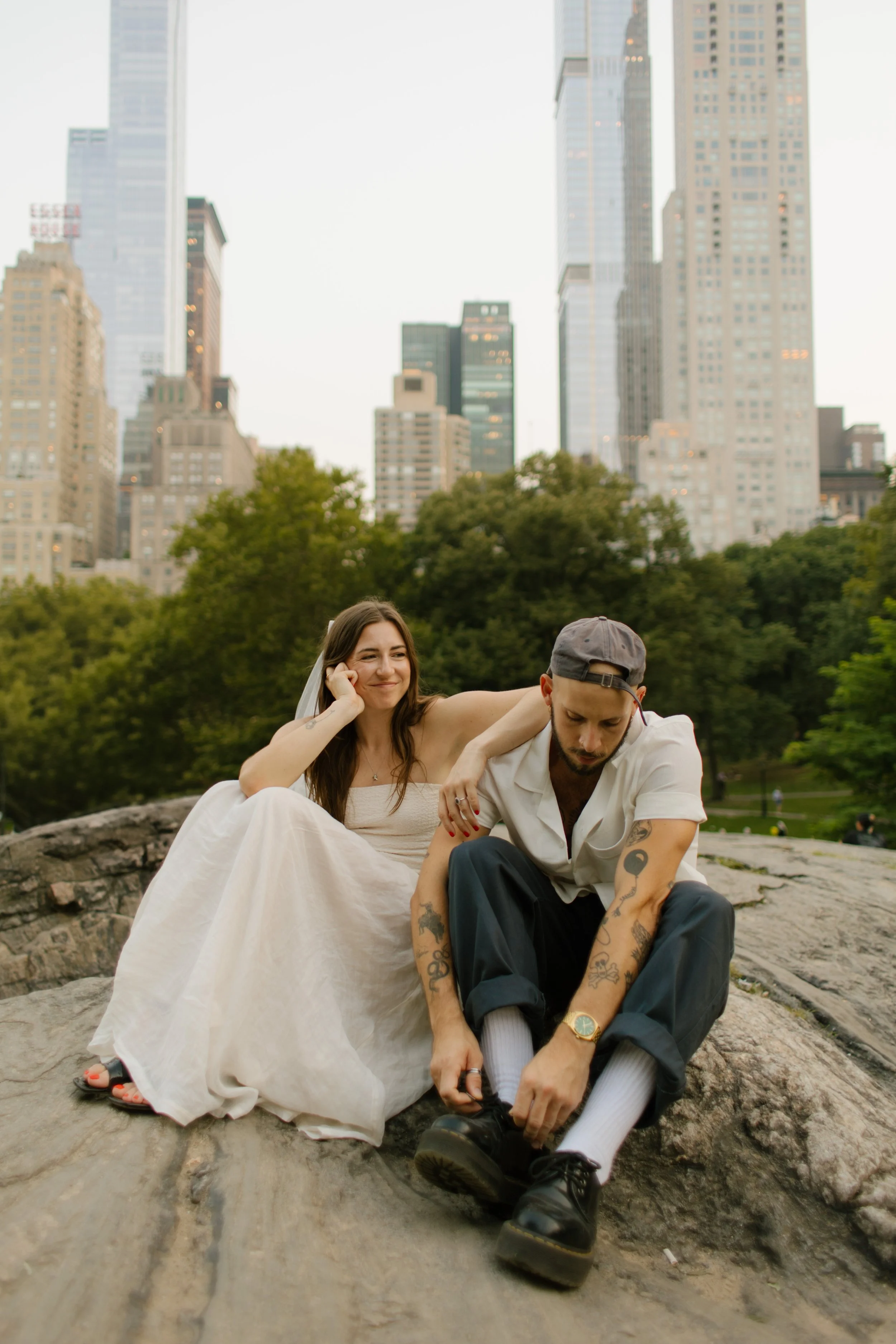 Couple sitting on a rock in Central Park with the Manhattan skyline behind them during an editorial engagement session.