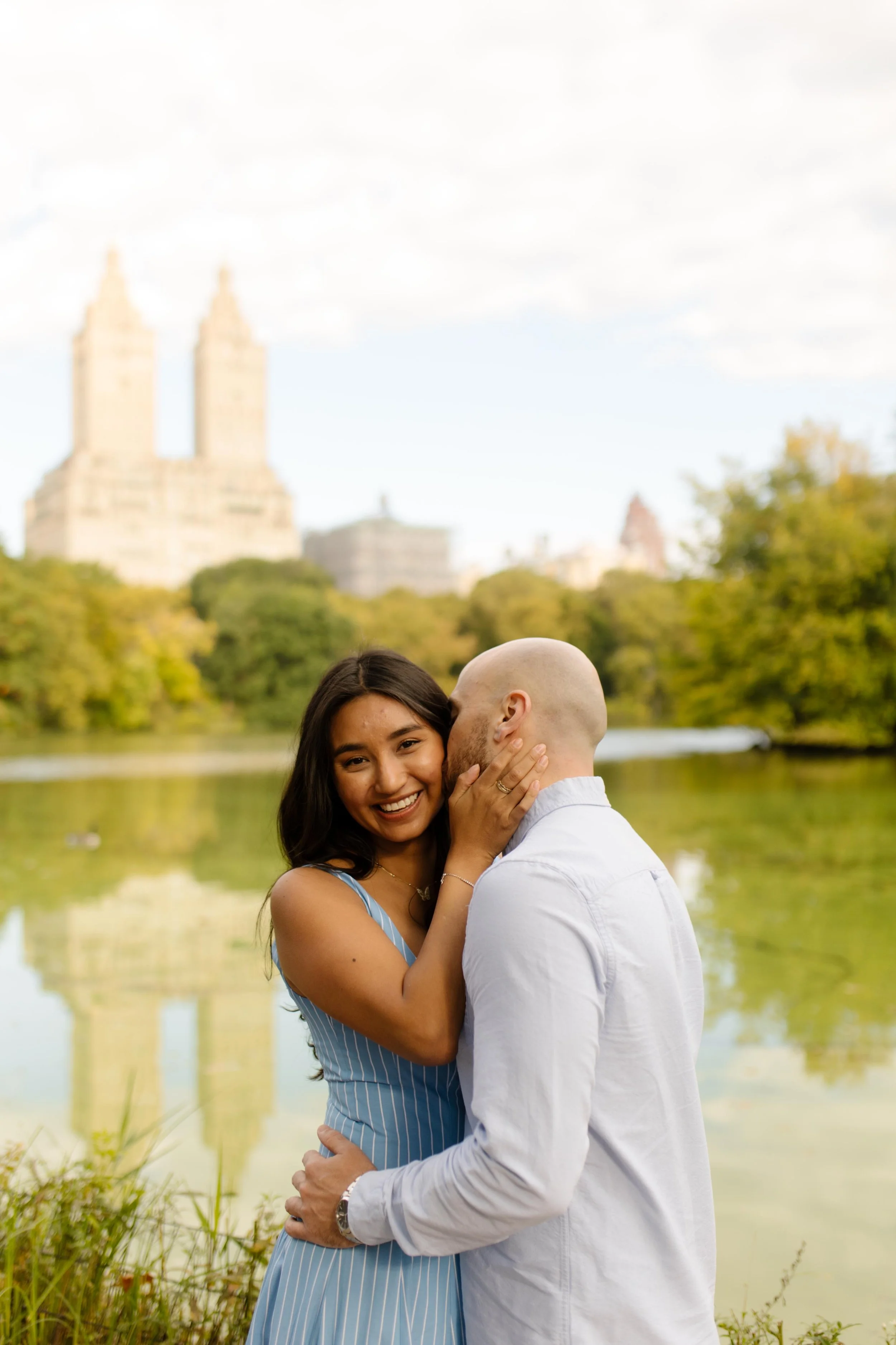 New York engagement photographer capturing a romantic lakeside portrait in Central Park with the city skyline in the background.