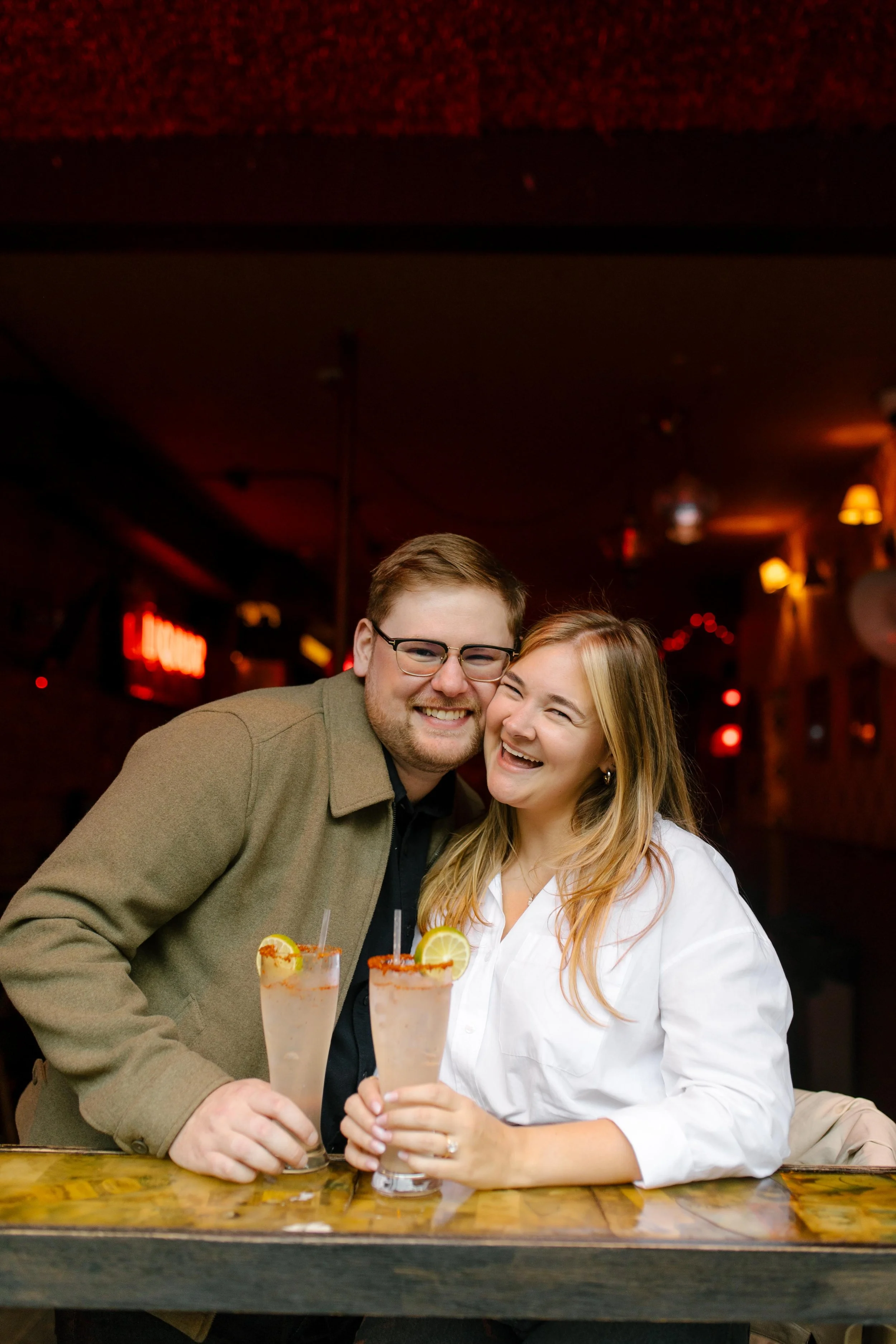 Couple laughing together over cocktails at a cozy neighborhood bar during a New York City engagement session.