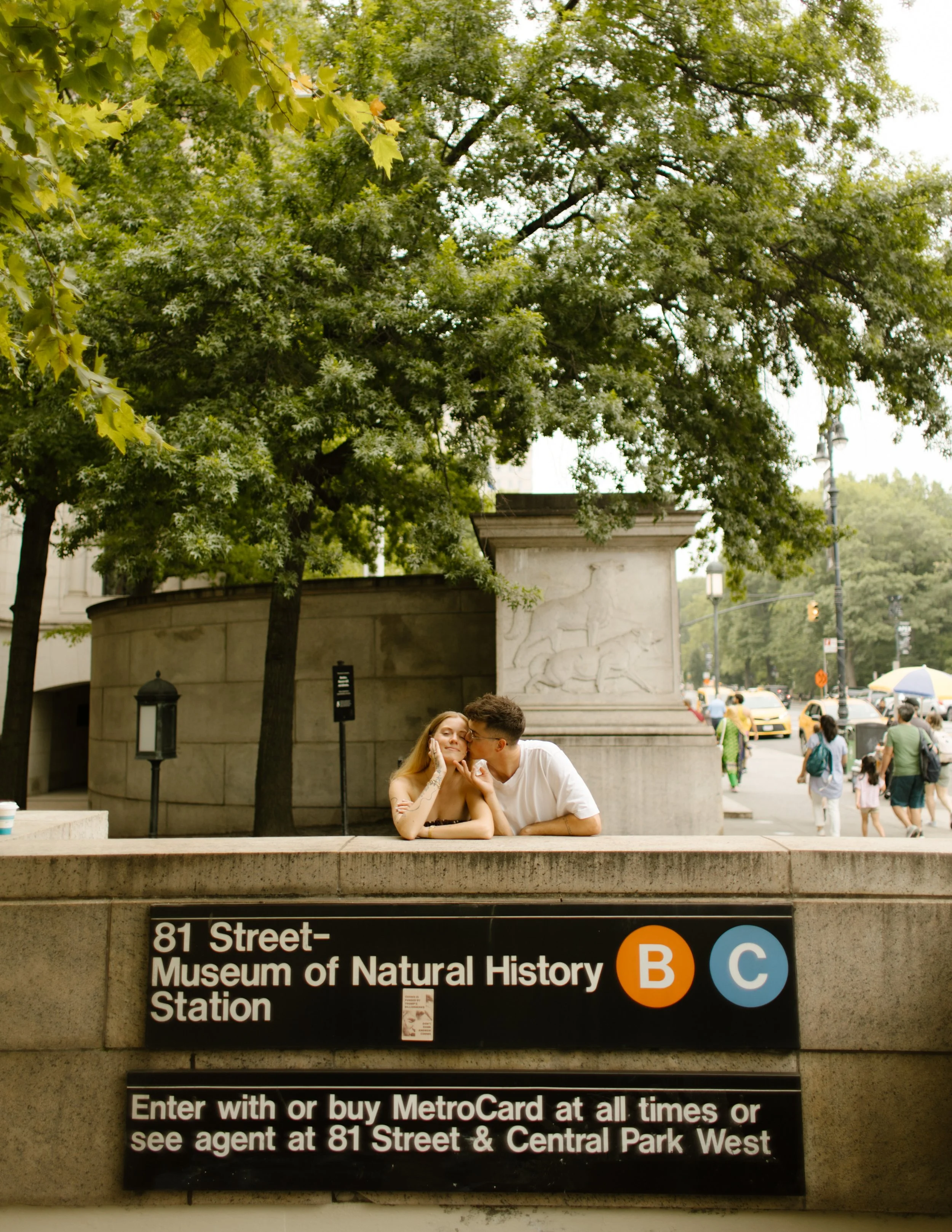 Couple leaning over the Museum of Natural History subway entrance during a playful Upper West Side engagement session.