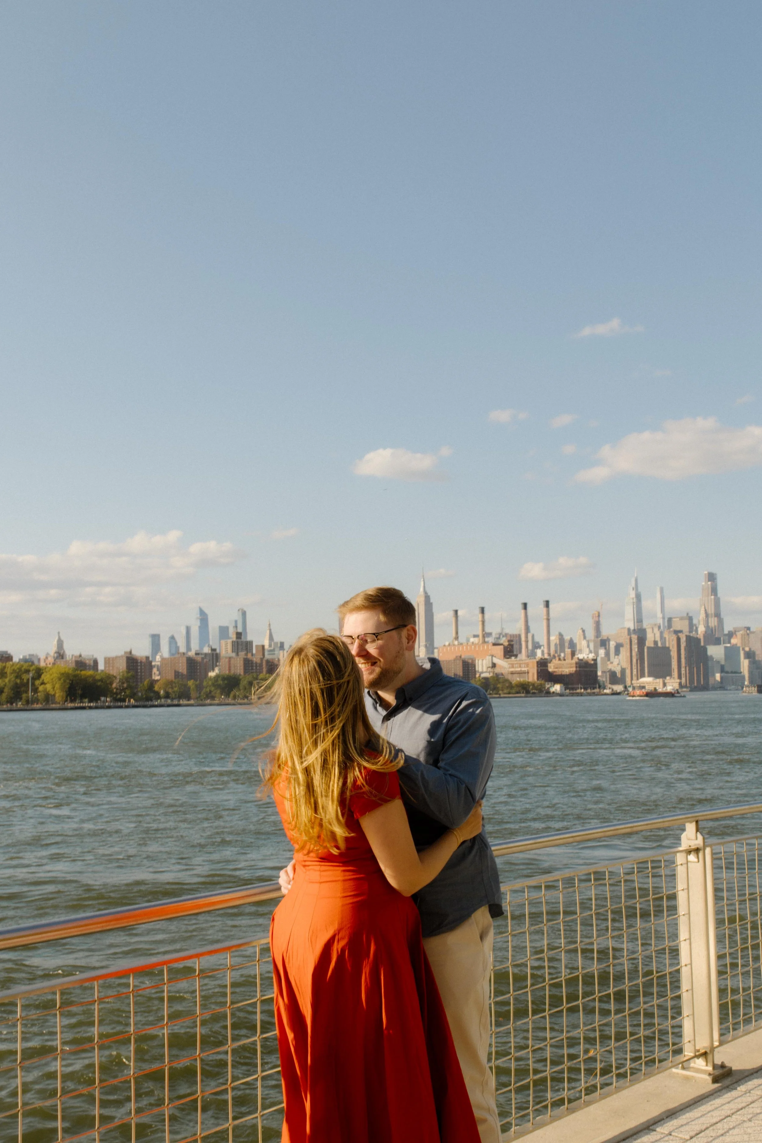 New York engagement photographer photographing a couple embracing along the Williamsburg waterfront with the Manhattan skyline behind them.