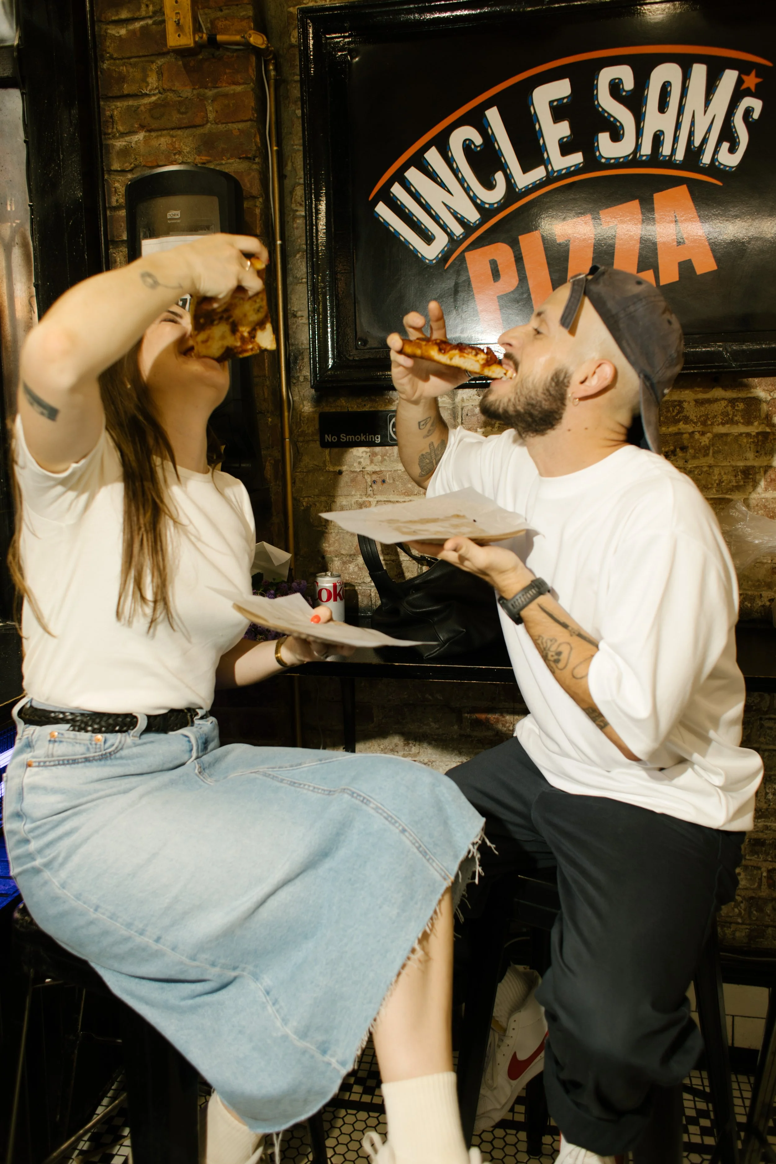 Couple laughing together outside a Manhattan bagel shop during a casual city engagement shoot.