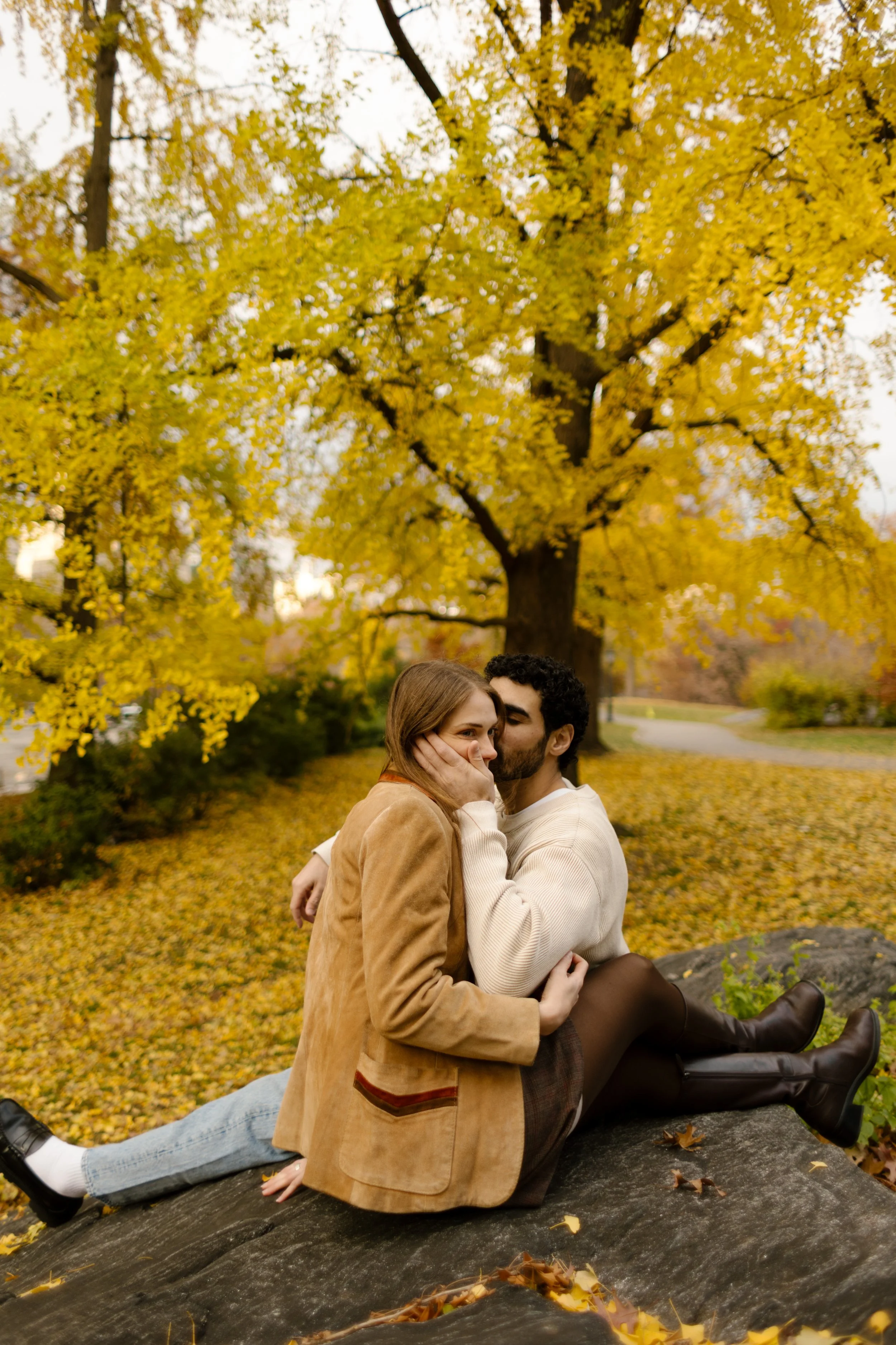Couple cuddling beneath golden autumn trees in Central Park during a romantic engagement session.