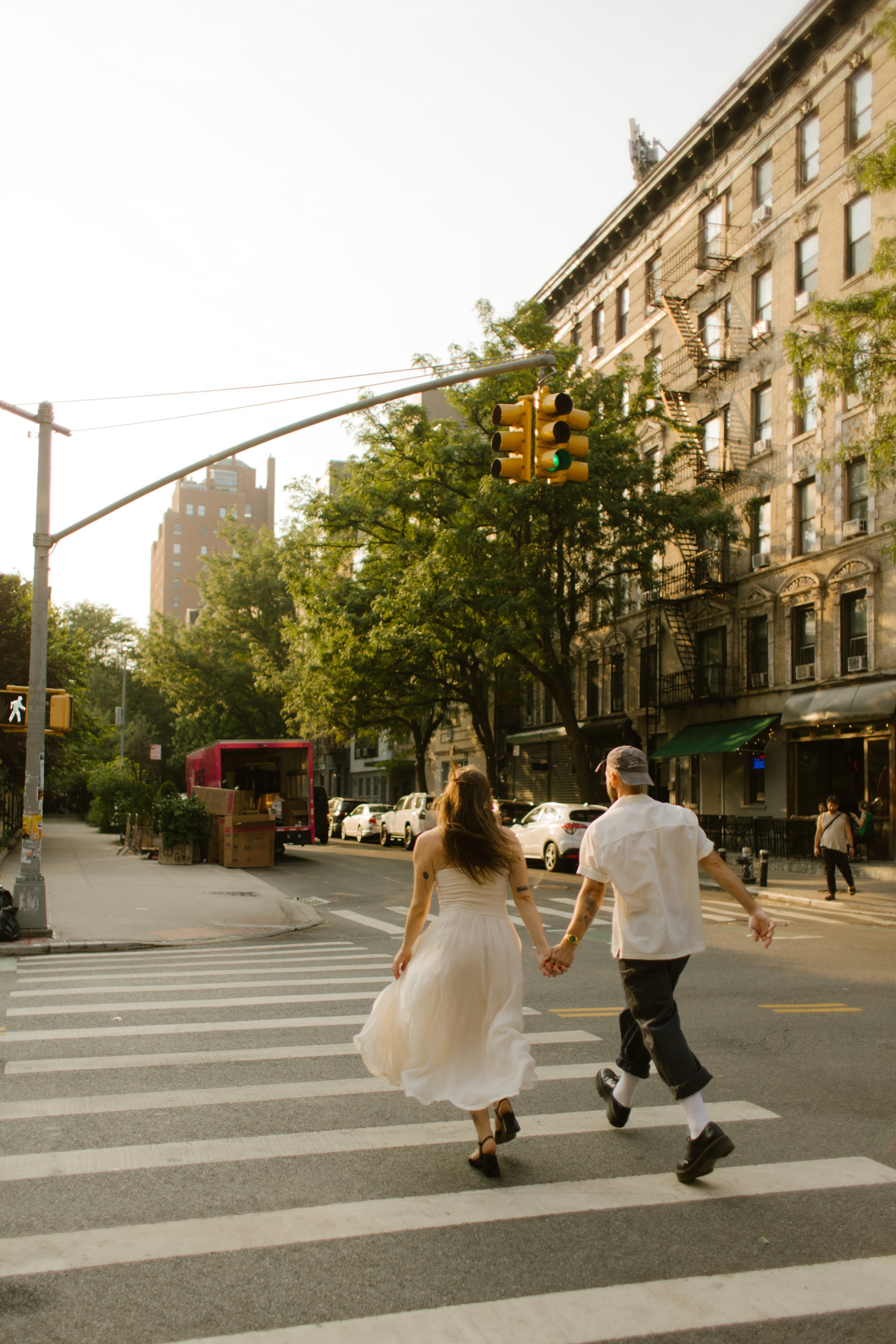 Couple running hand in hand across a quiet New York City street at golden hour.