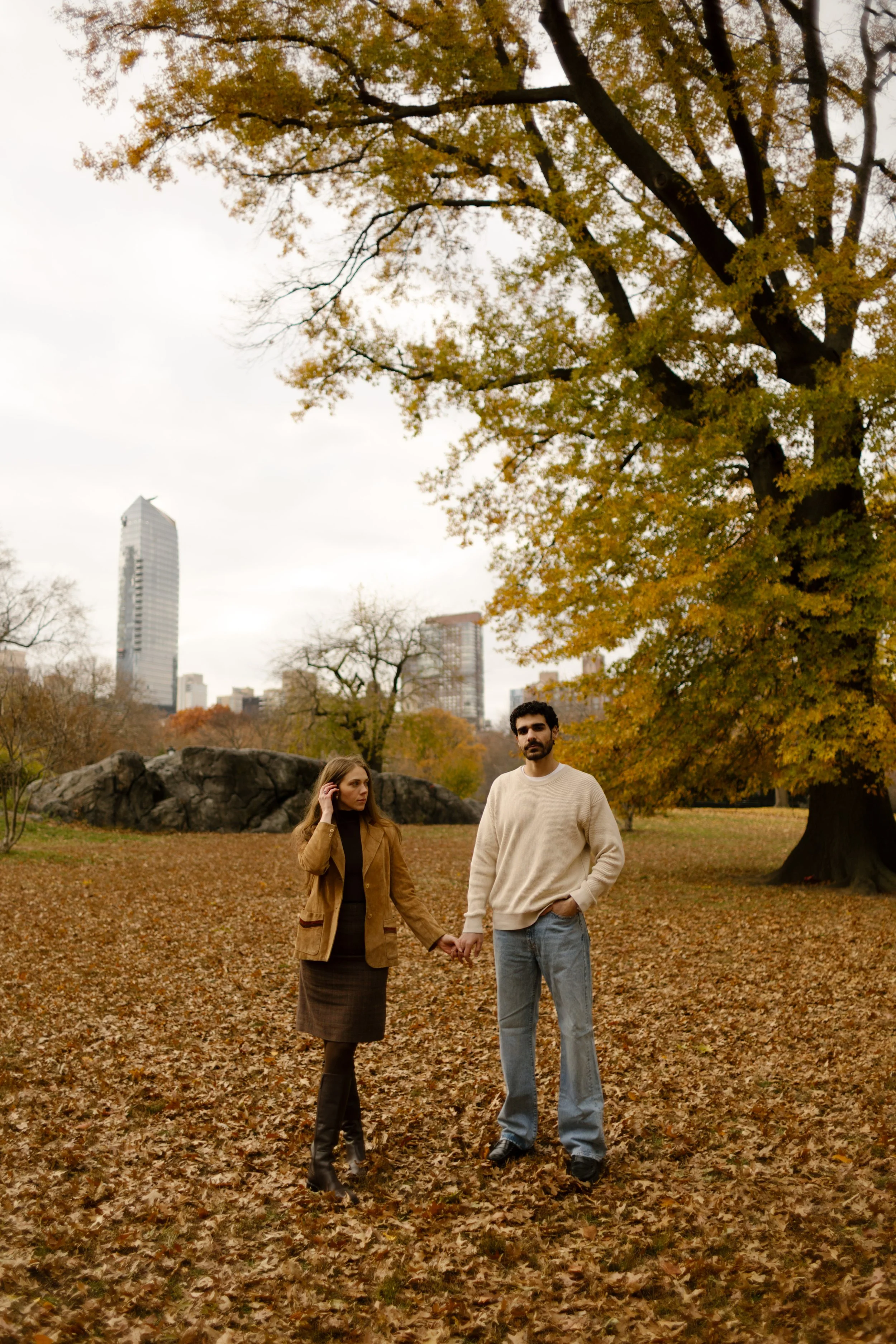 New York engagement photographer capturing a couple holding hands in Central Park surrounded by autumn leaves.