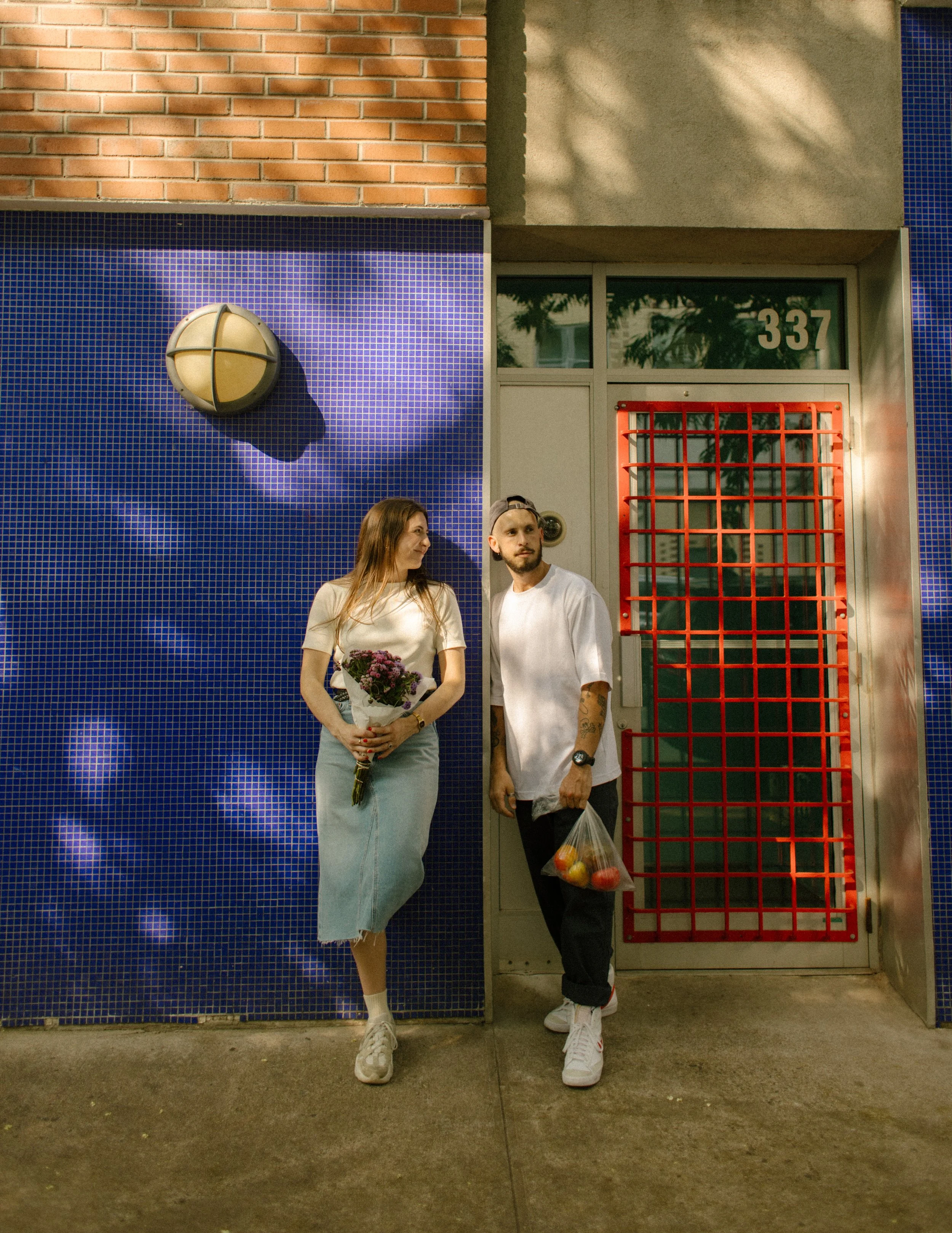 Couple posing with flowers and fresh produce outside a colorful Manhattan storefront during an engagement session.