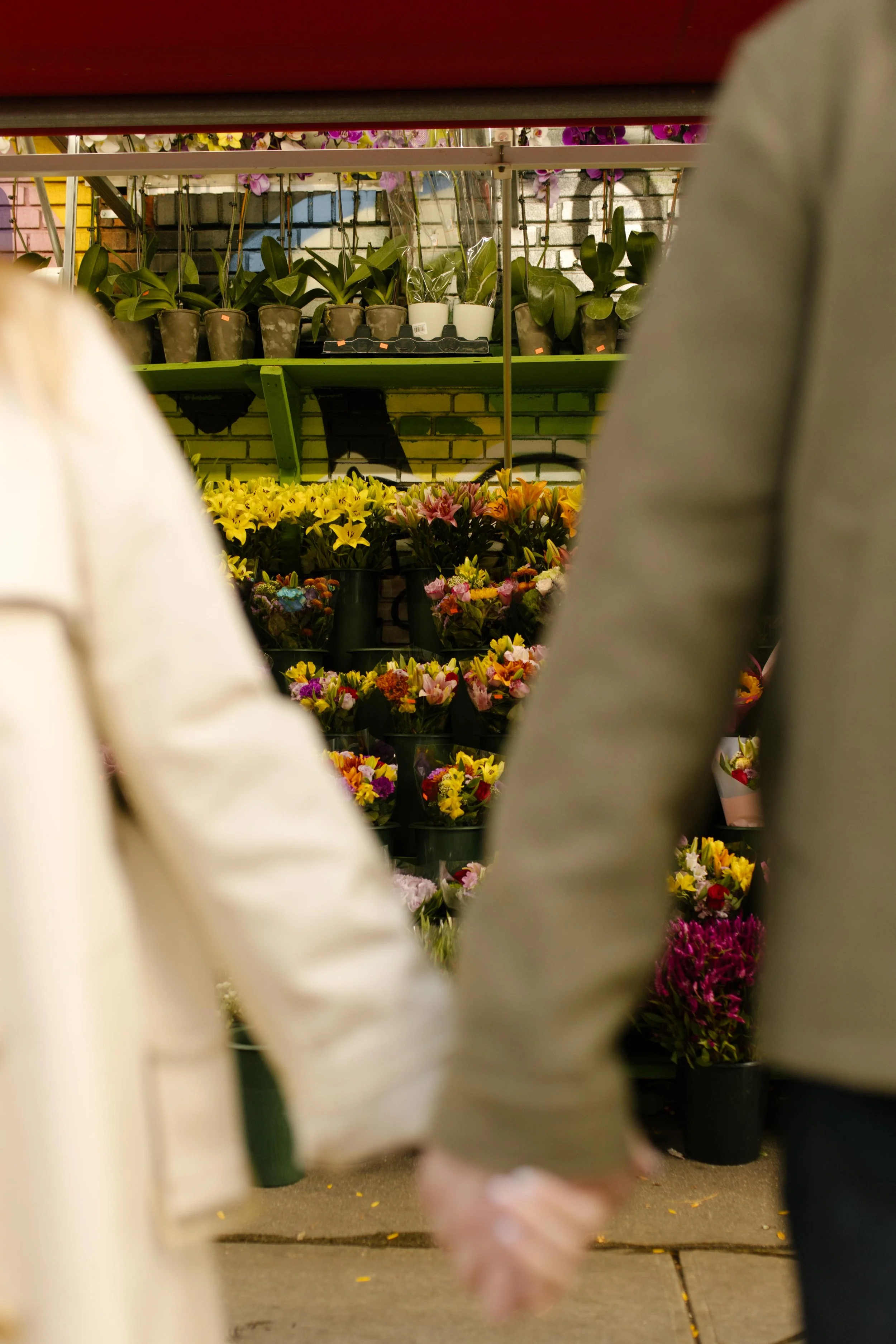 Close-up of a couple holding hands in front of a vibrant New York flower stand filled with fresh blooms