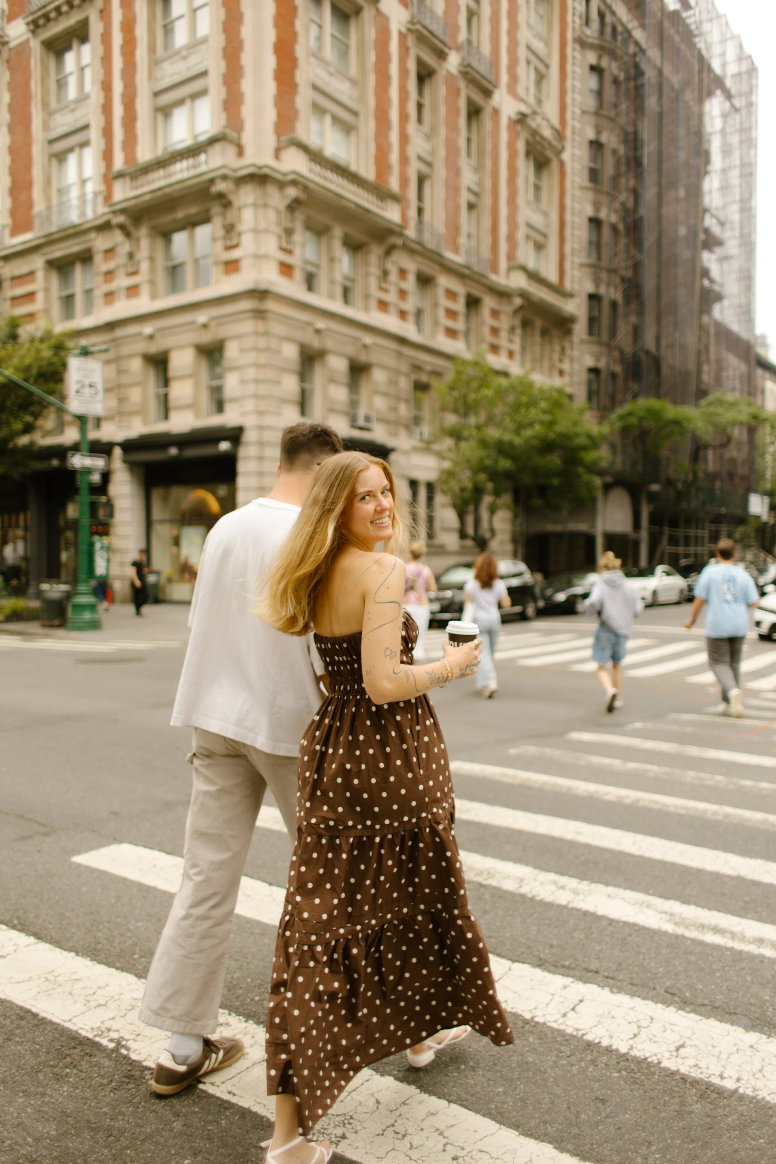 Couple walking across the street holding hands while the woman looks over her shoulder.