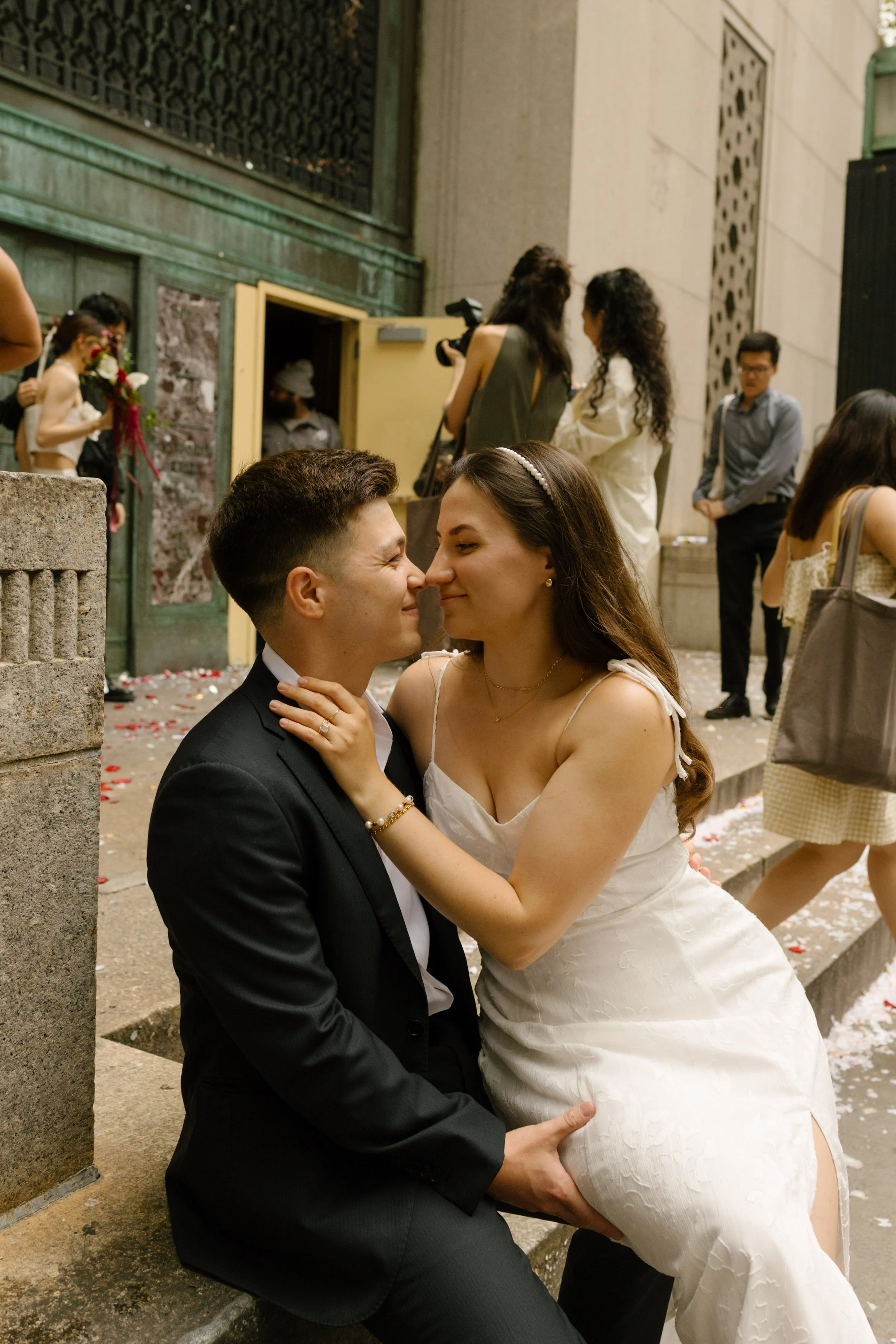 Newlyweds embracing outside Manhattan ceremony venue surrounded by flower petals and guests