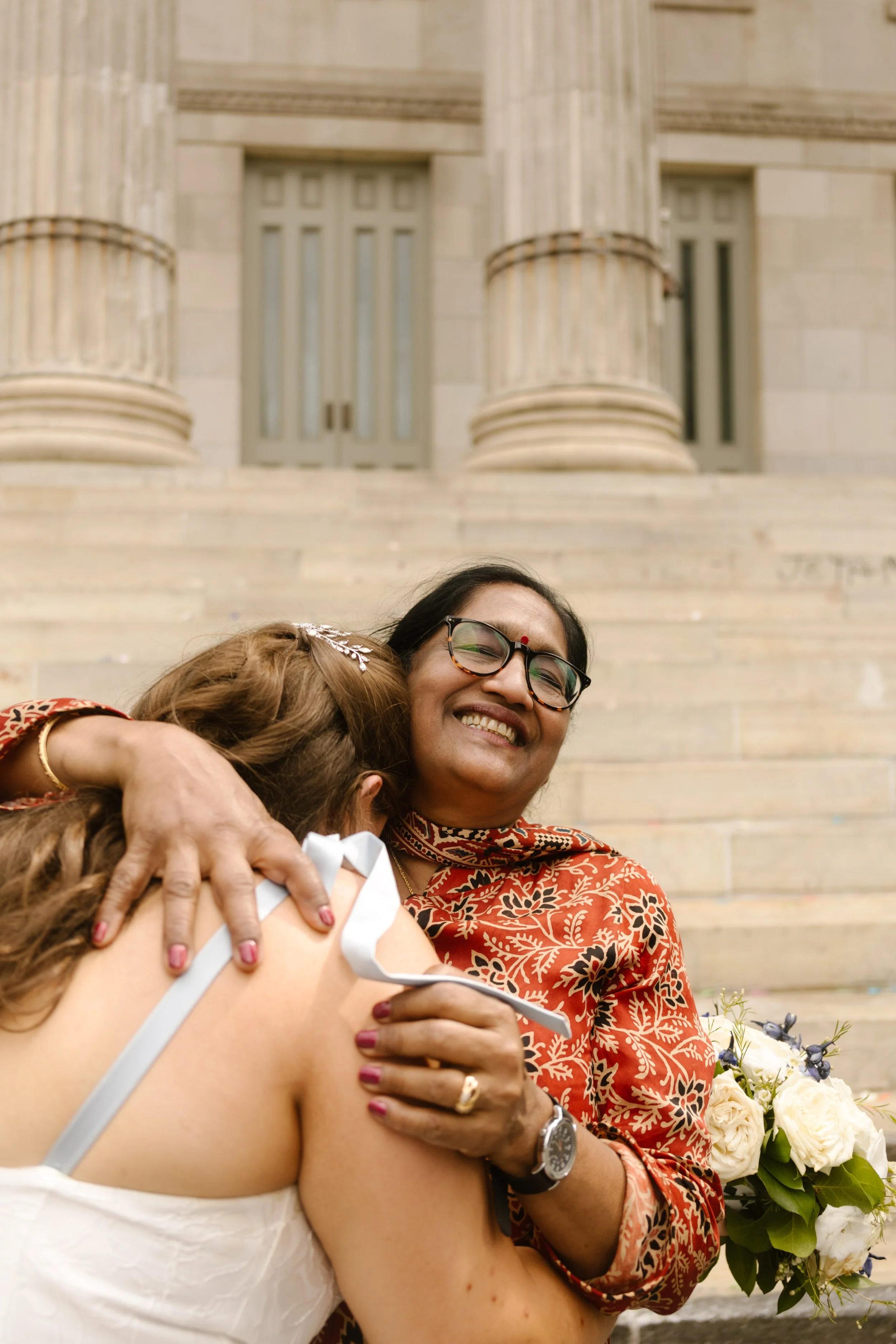 Emotional embrace between wedding guest and bride outside grand Manhattan courthouse steps
