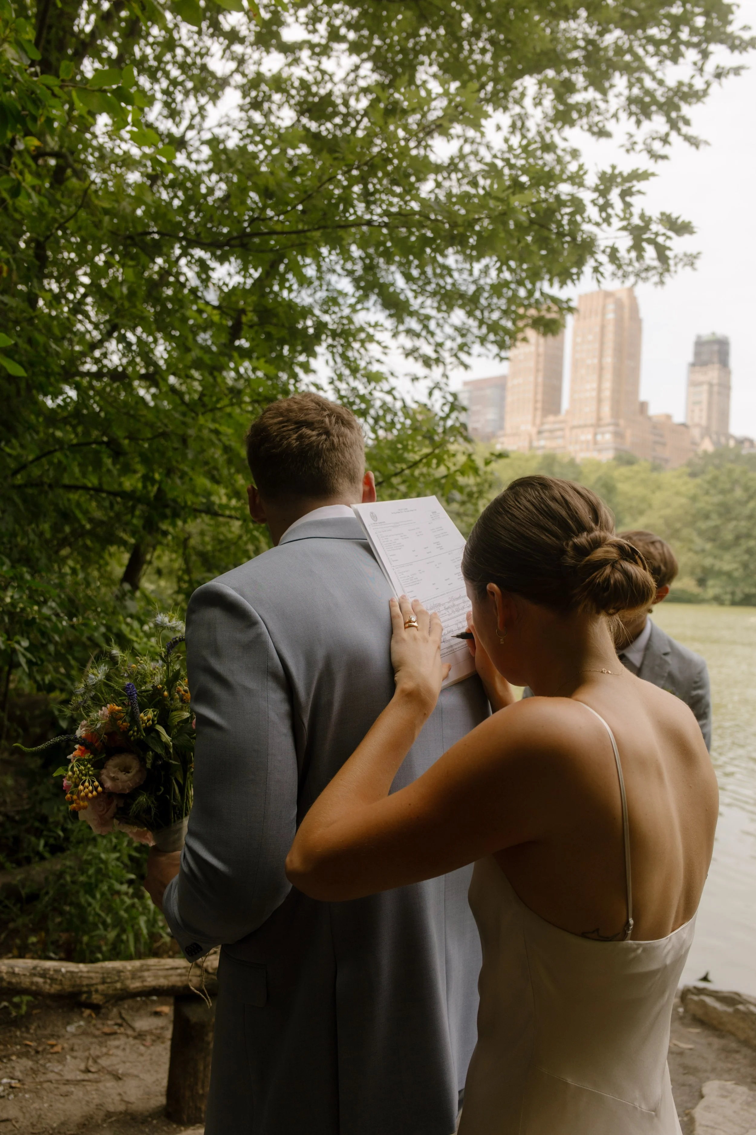 Bride reading handwritten vows beside lakeside ceremony setting in Central Park