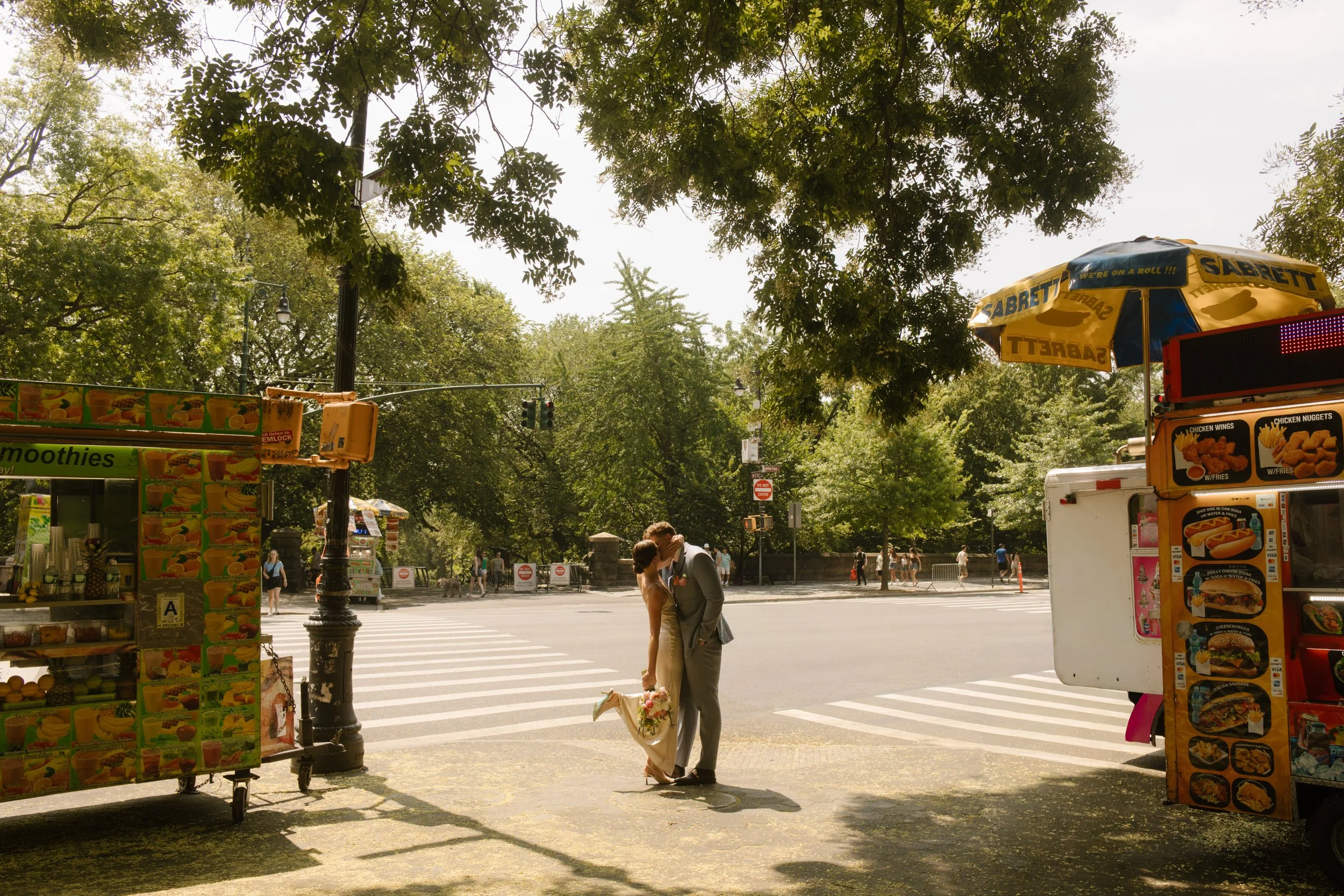 Bride and groom embracing in crosswalk beside Central Park food carts and city traffic