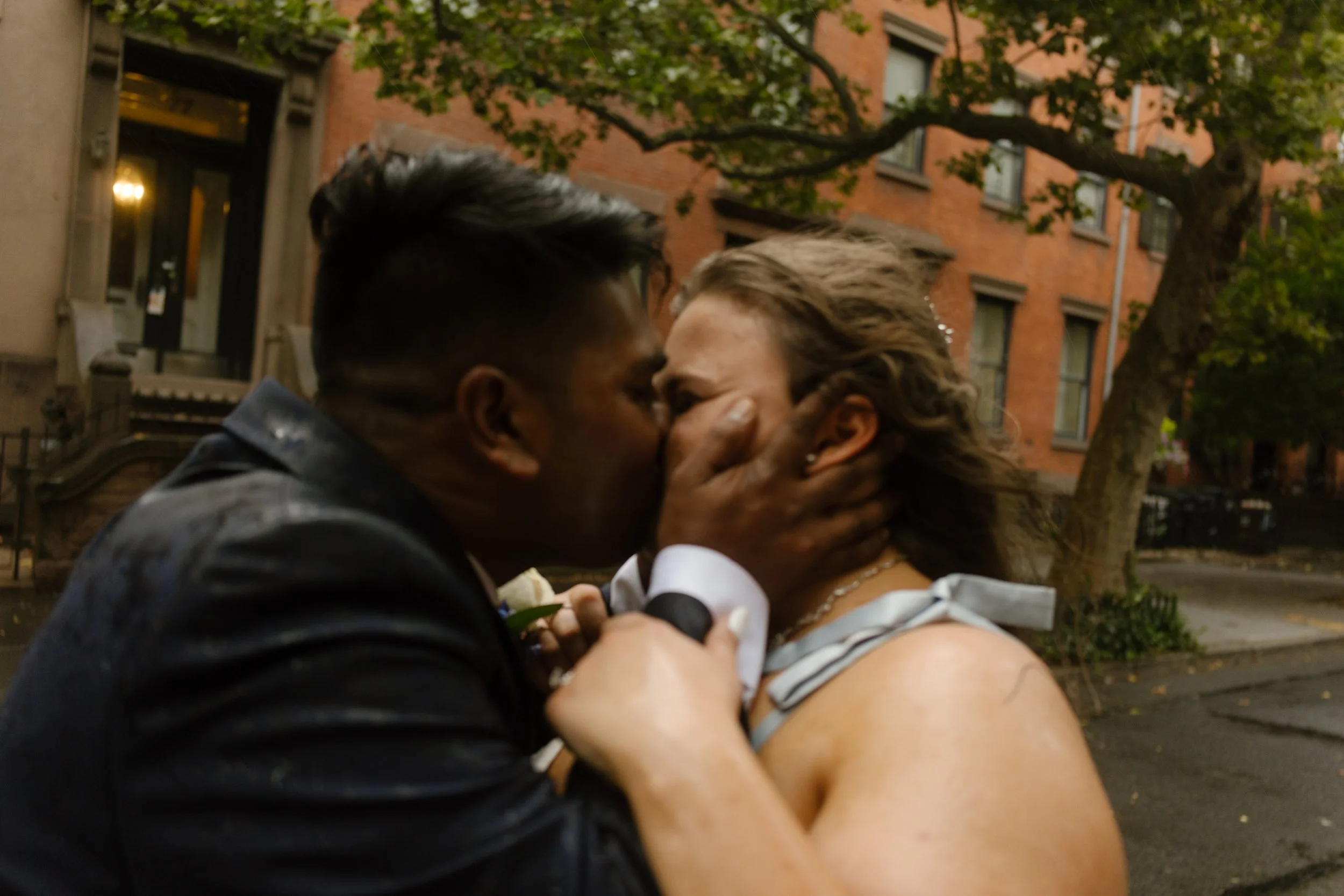 Emotional kiss between newlyweds on rainy Brooklyn brownstone street after ceremony