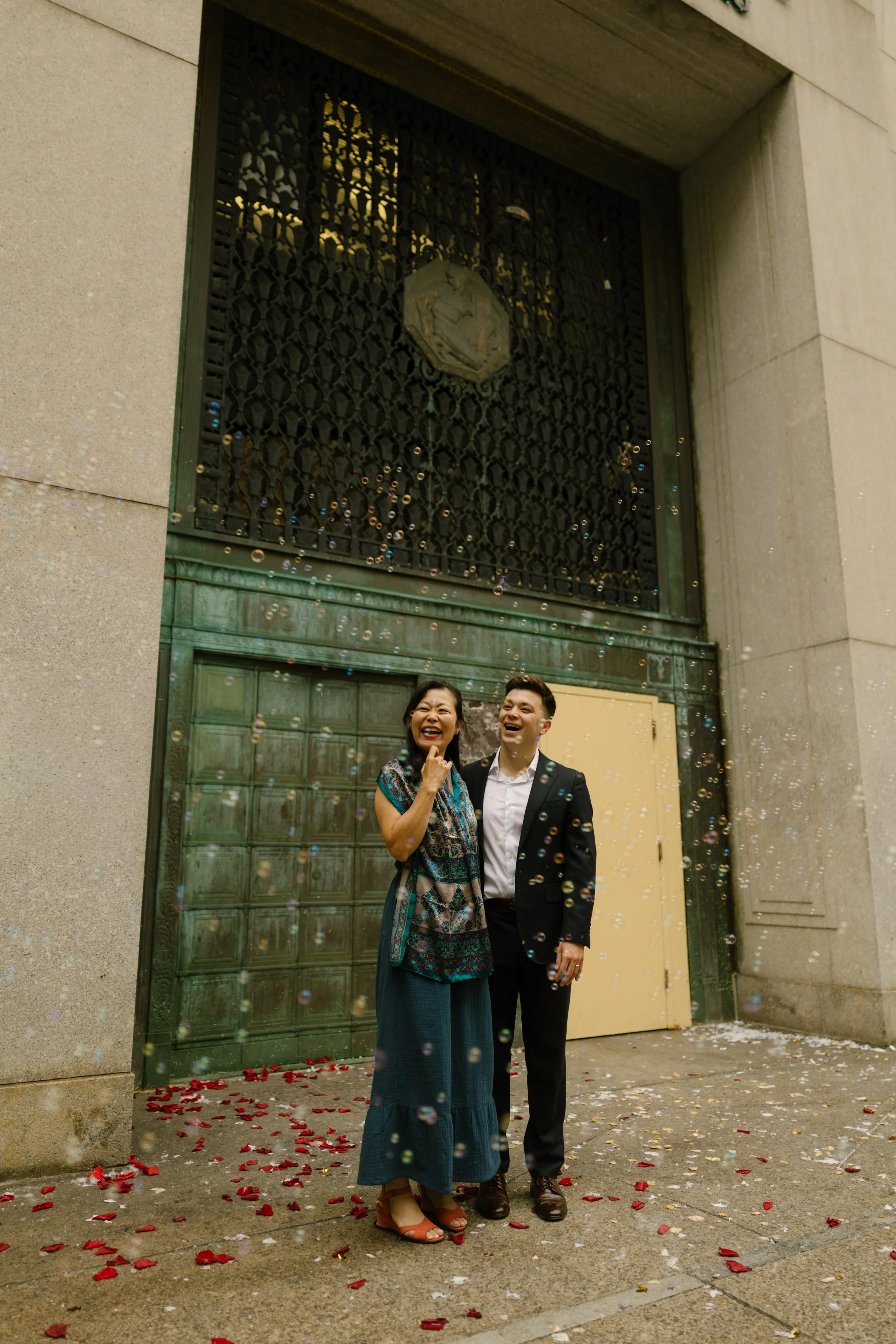 Family celebrating outside ceremony venue as flower petals and bubbles fill the street