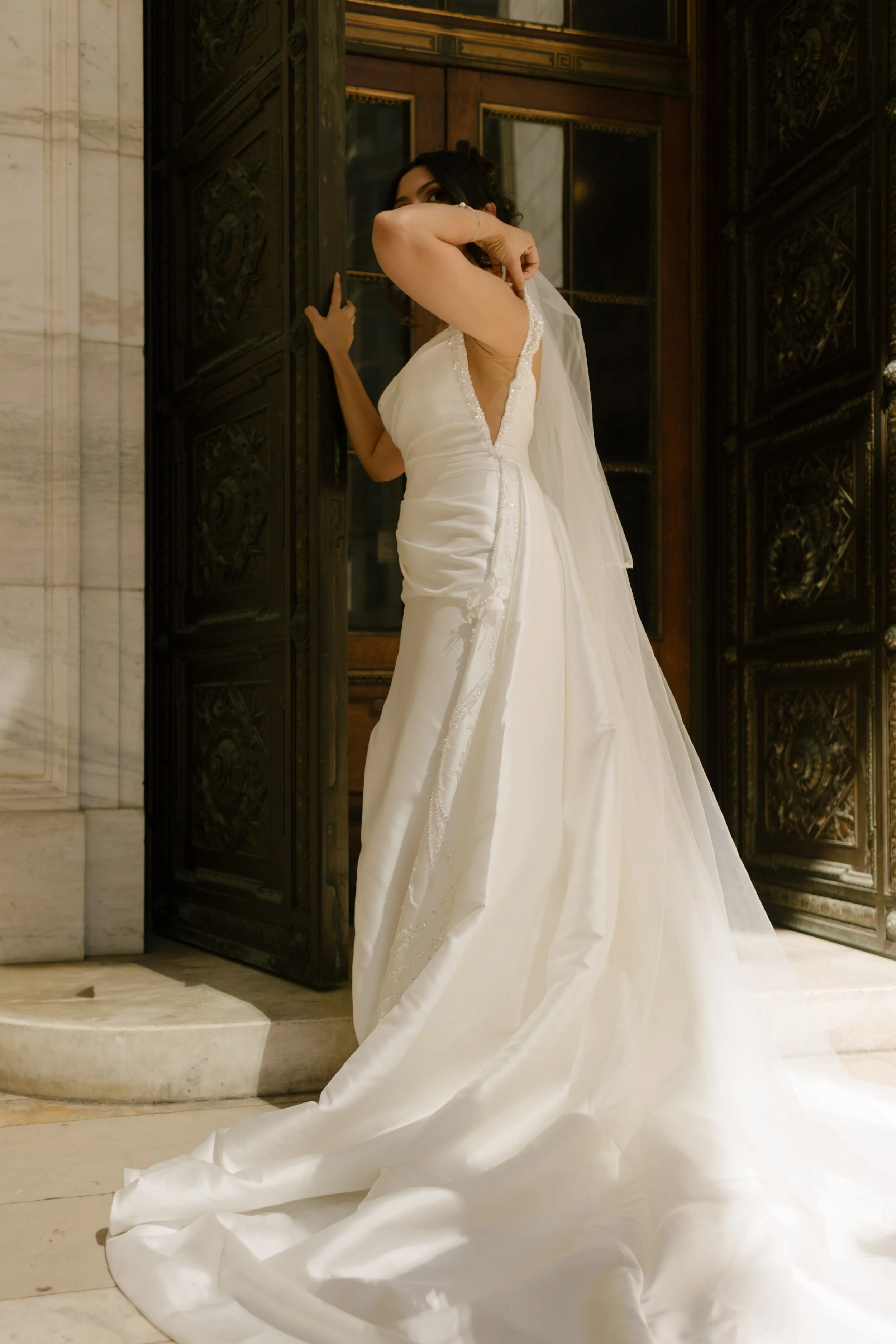 Bride adjusting veil outside grand Manhattan building during elegant New York Wedding portraits