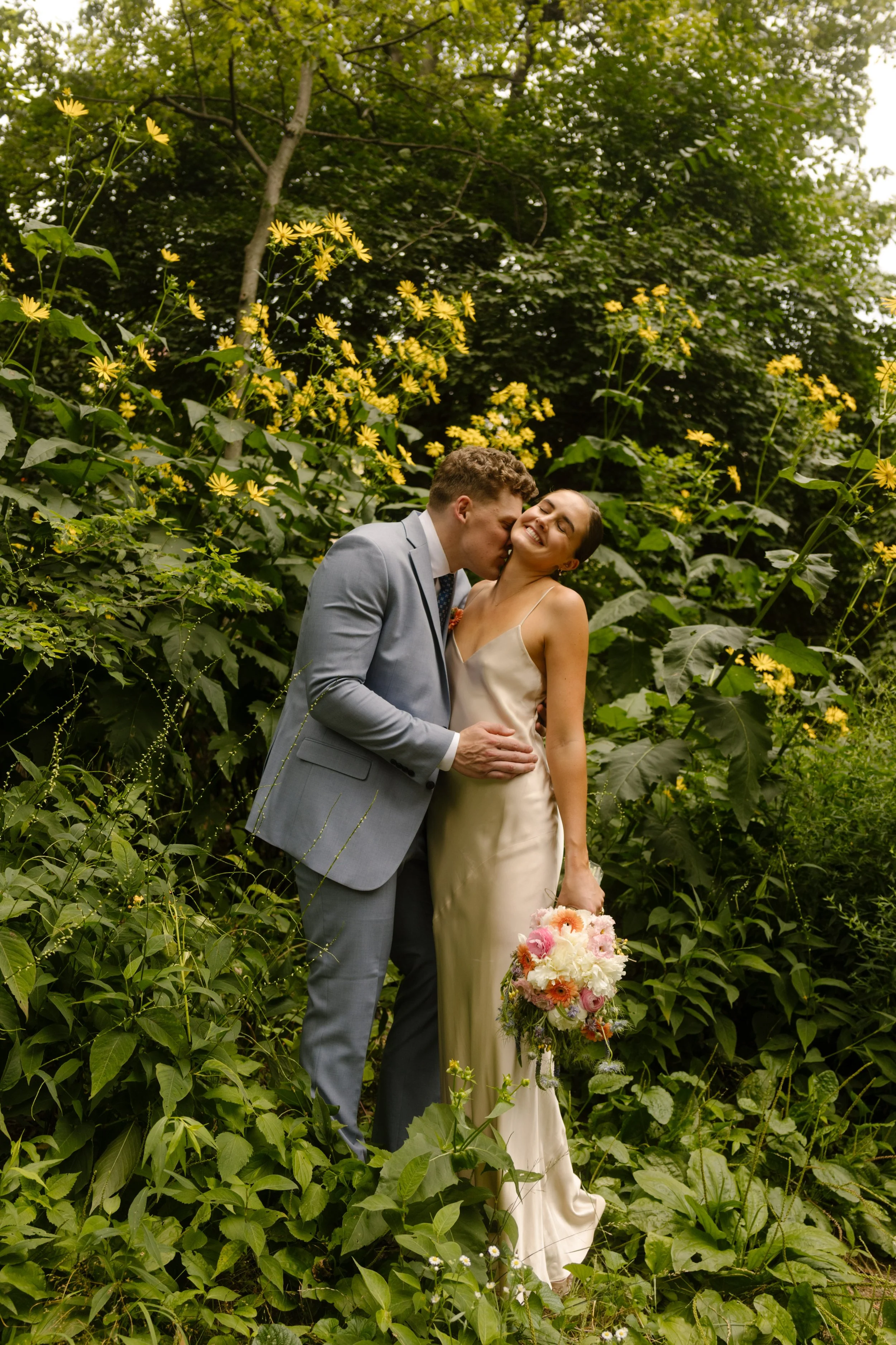 Bride and groom embracing in lush Central Park greenery during romantic portrait session
