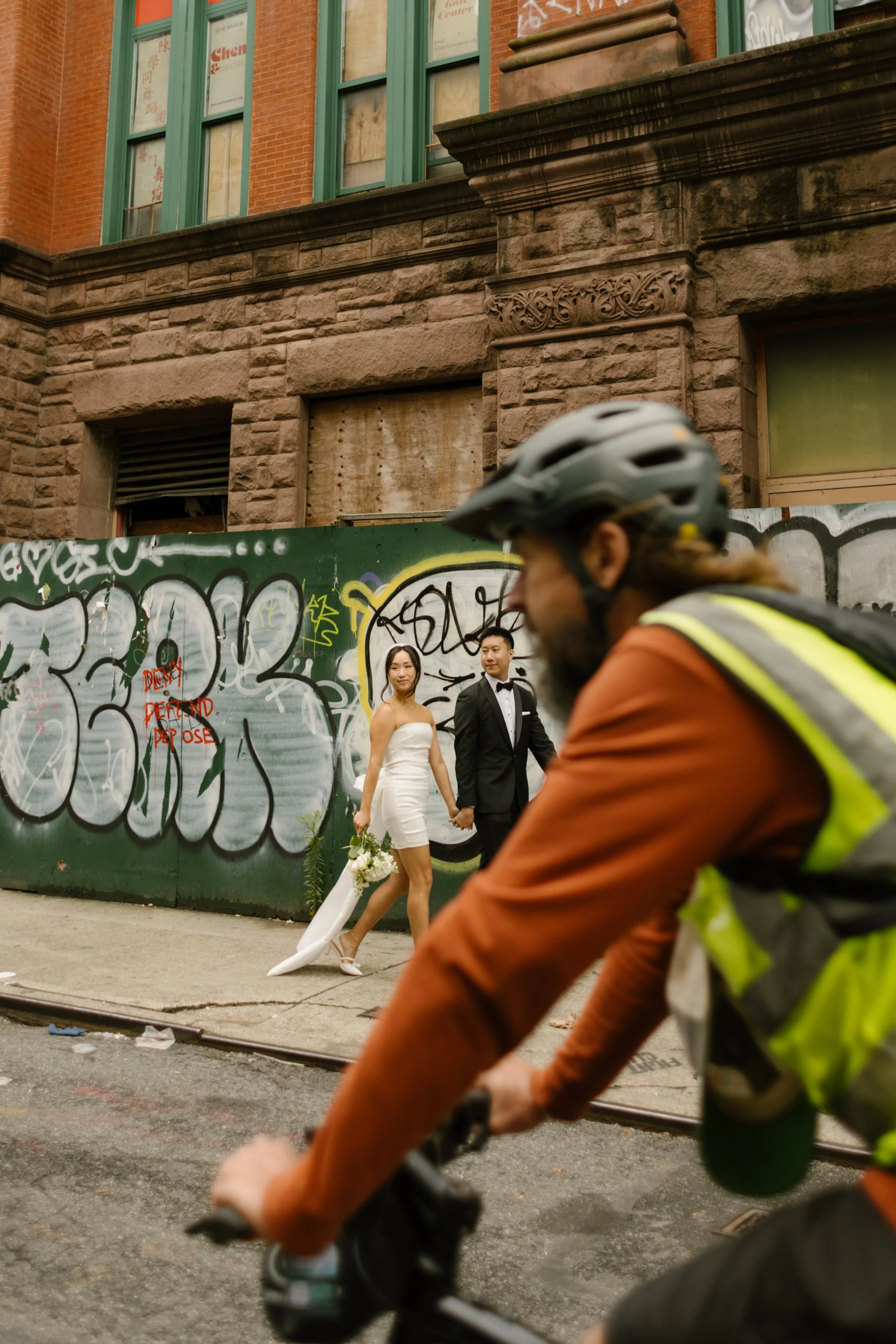 Stylish couple walking through SoHo street with cyclist passing during New York Wedding portraits