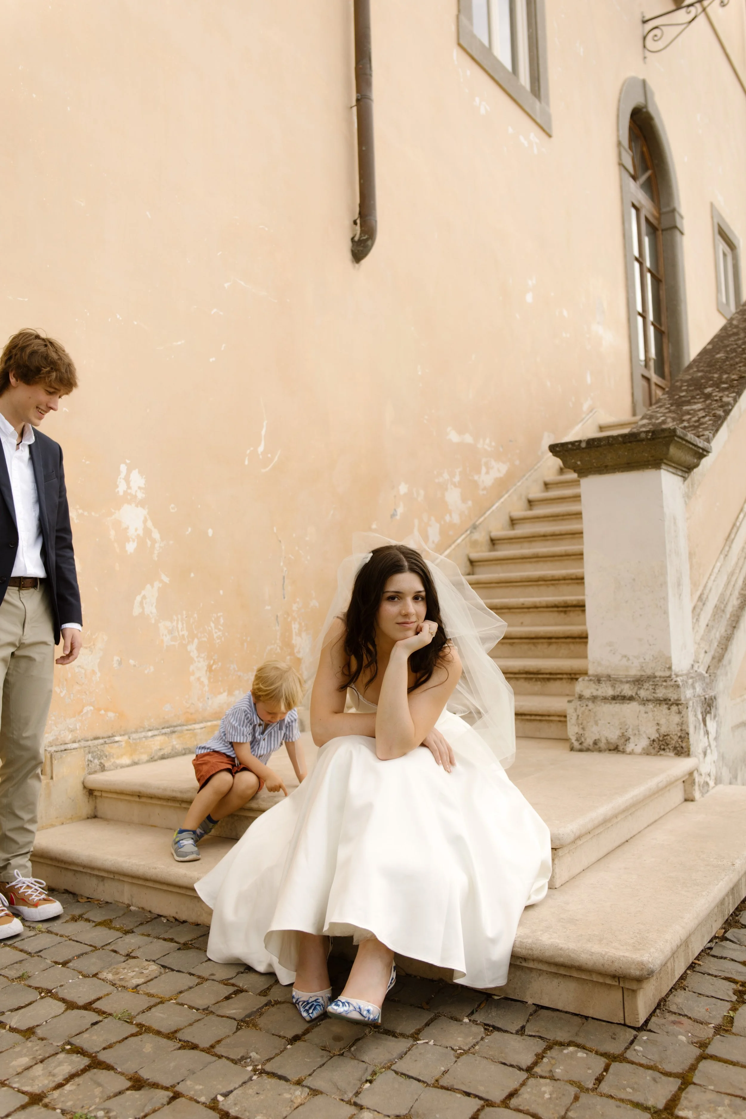 Bride sitting on villa steps with candid family moments happening around her during an Italy wedding weekend