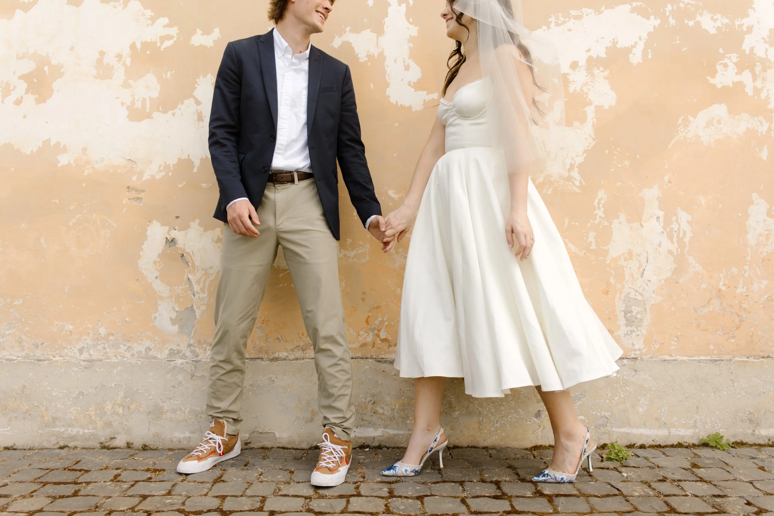 Bride and groom holding hands in front of a weathered villa wall during an Italy wedding weekend