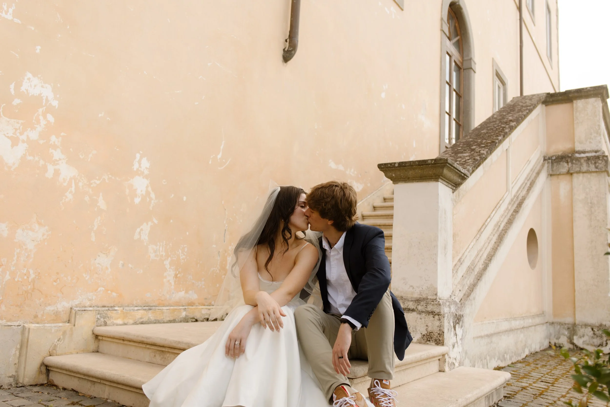Bride and groom kissing on stone stairs outside an Italian villa during their destination wedding in Italy