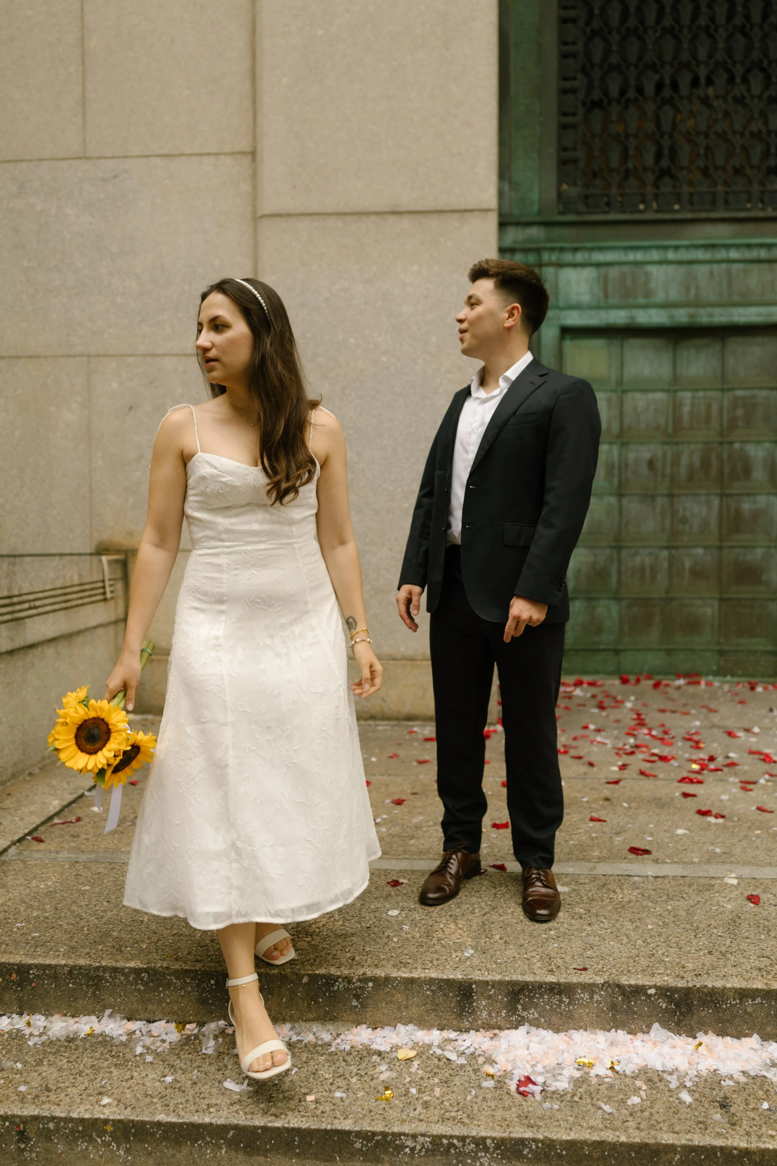 Newly married couple standing on courthouse steps with flower petals scattered around them