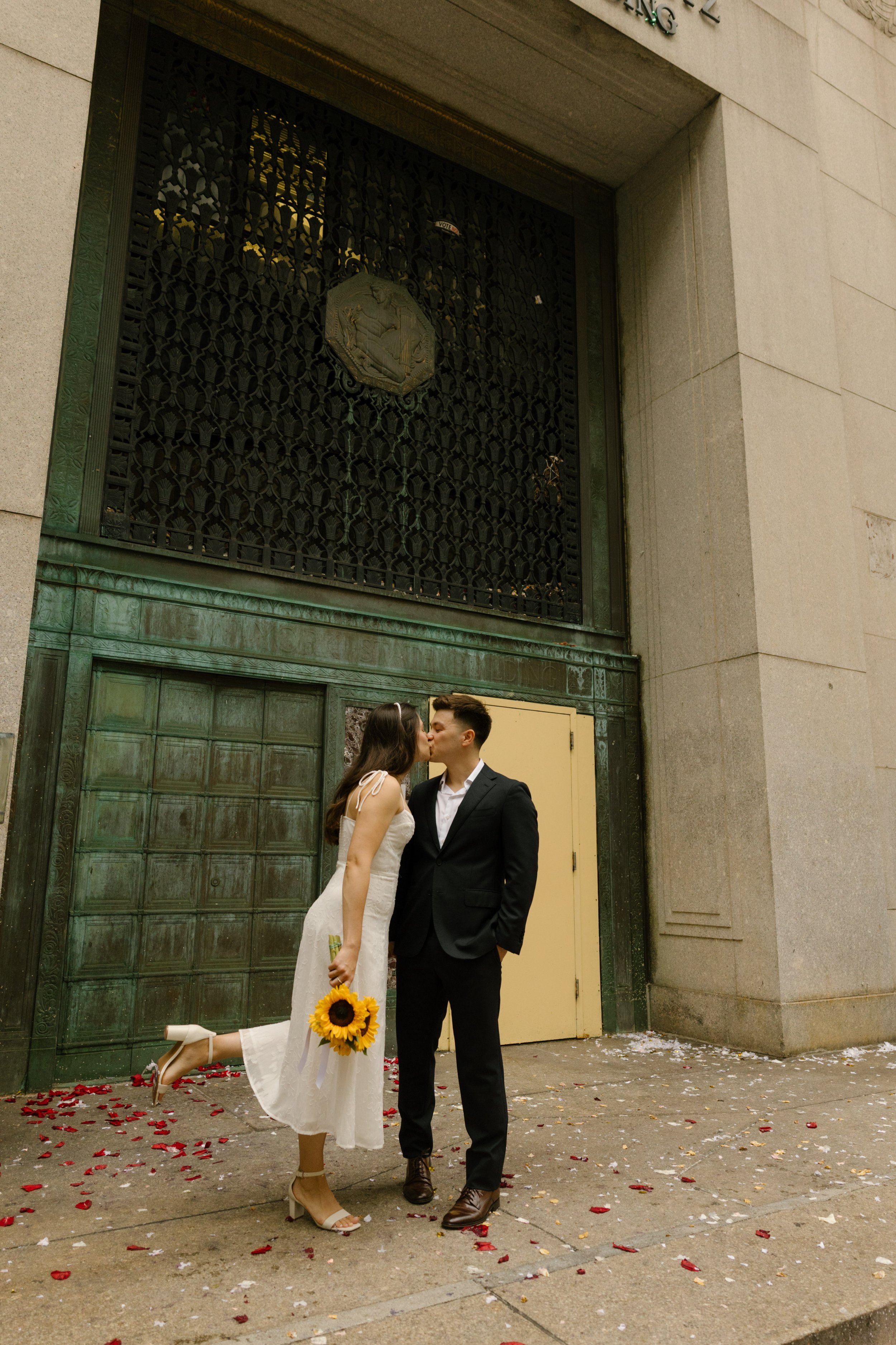 Bride and groom kissing outside NYC City Hall holding sunflower bouquet after courthouse ceremony