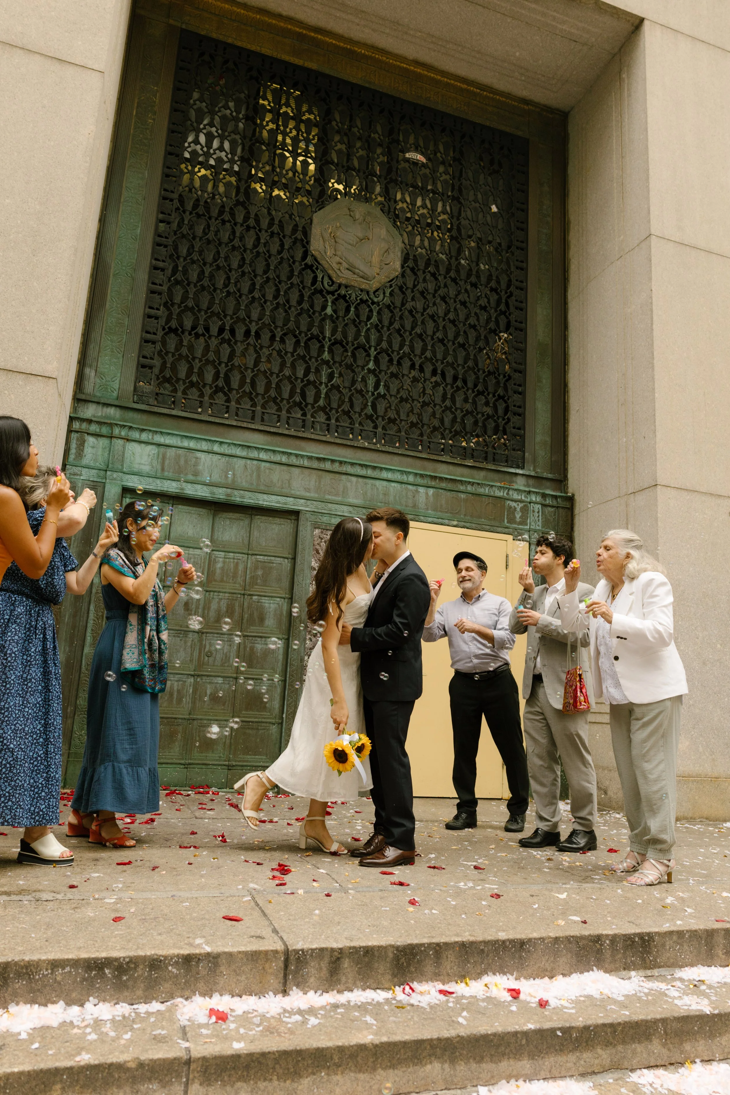 Bride and groom kissing outside courthouse while guests celebrate with bubbles