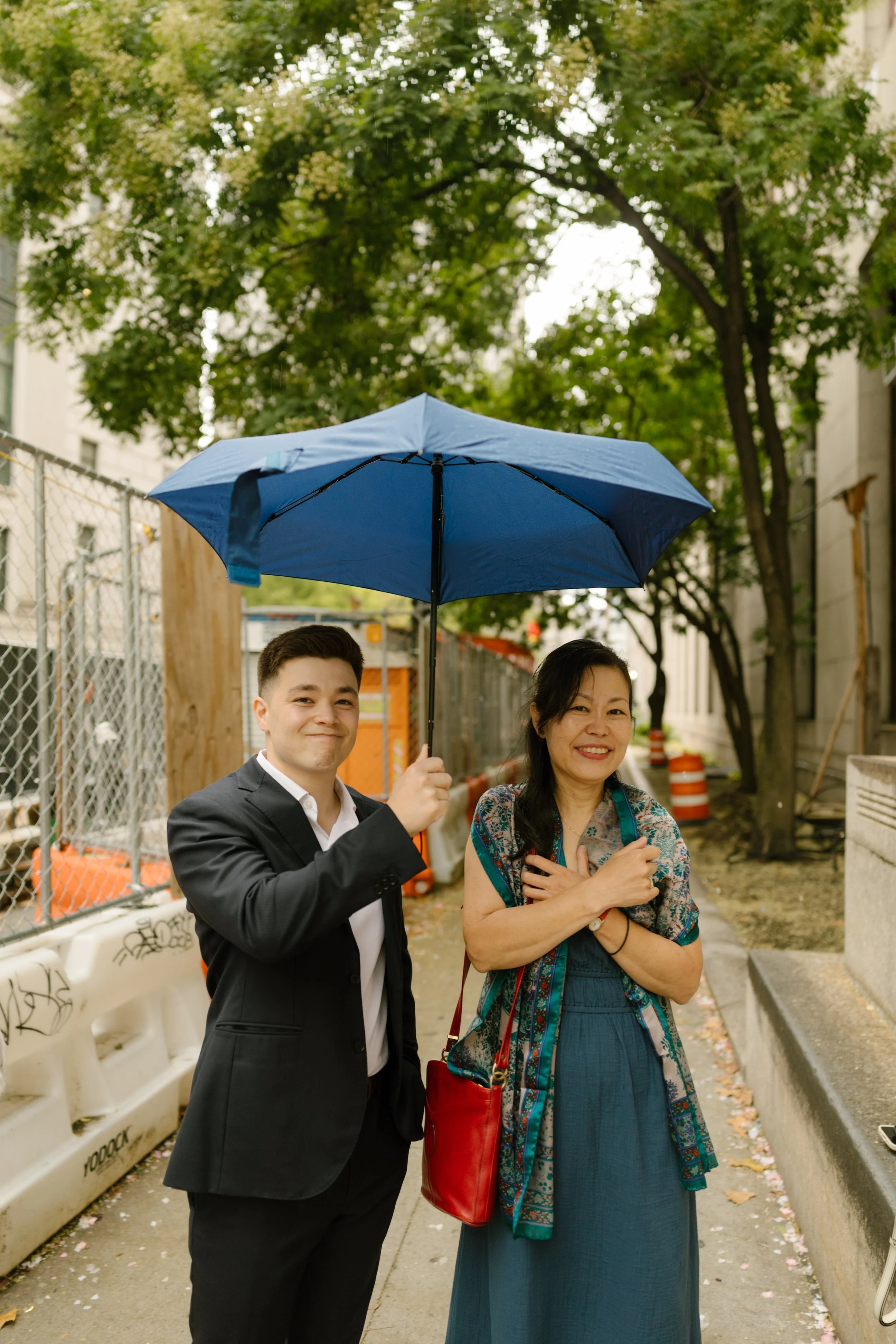 Wedding guests standing with groom under umbrella before New York courthouse wedding. 