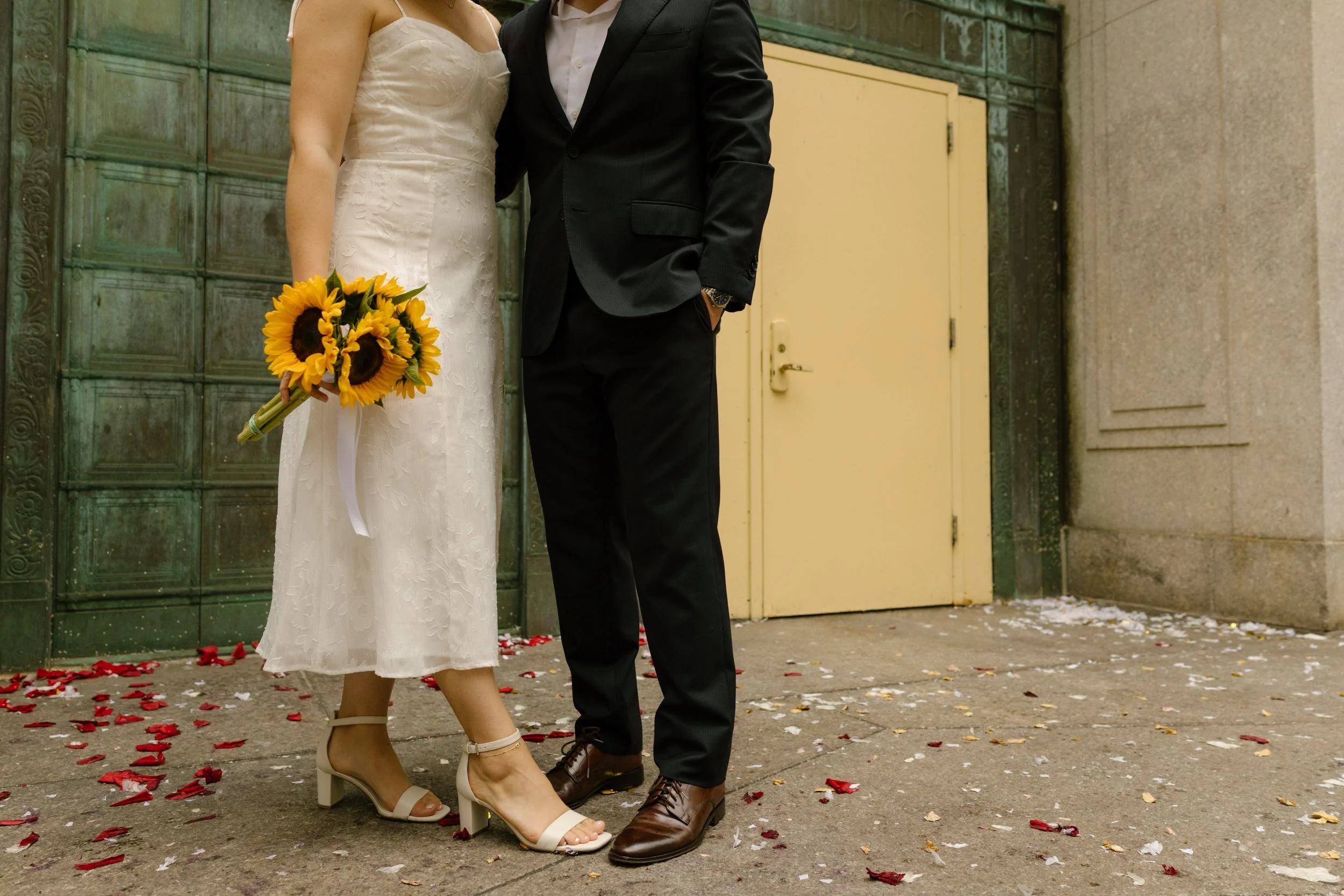 Bride holding a sunflower bouquet beside groom outside the courthouse following their New York courthouse wedding.