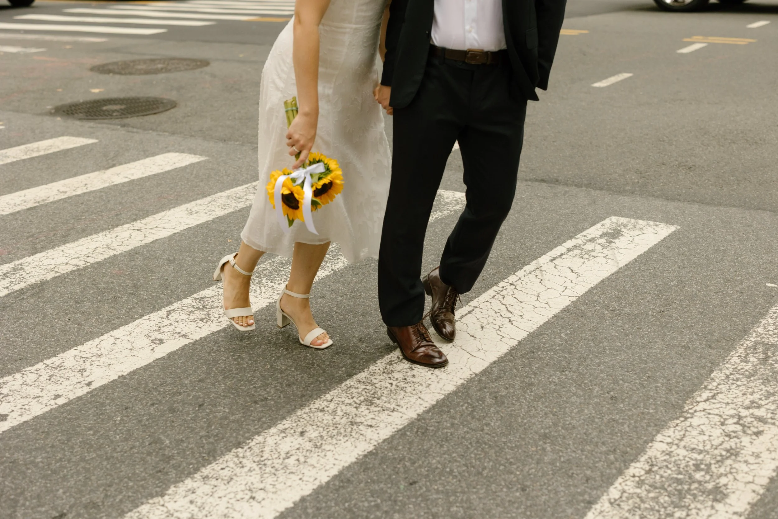 Couple crossing a Manhattan street after their New York courthouse wedding with bouquet and wedding attire