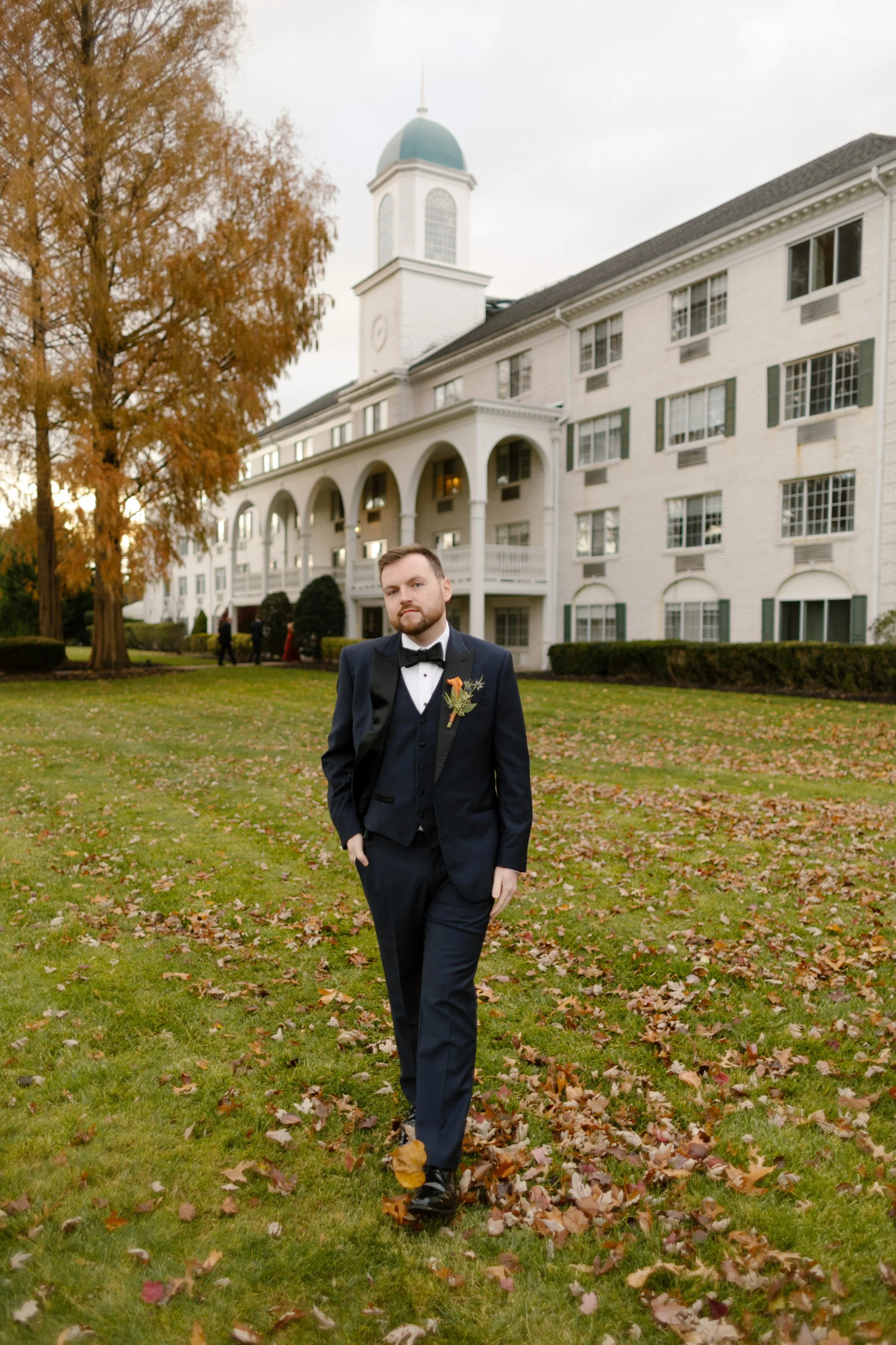 Groom portrait on the lawn outside a historic hotel venue during a fall wedding celebration