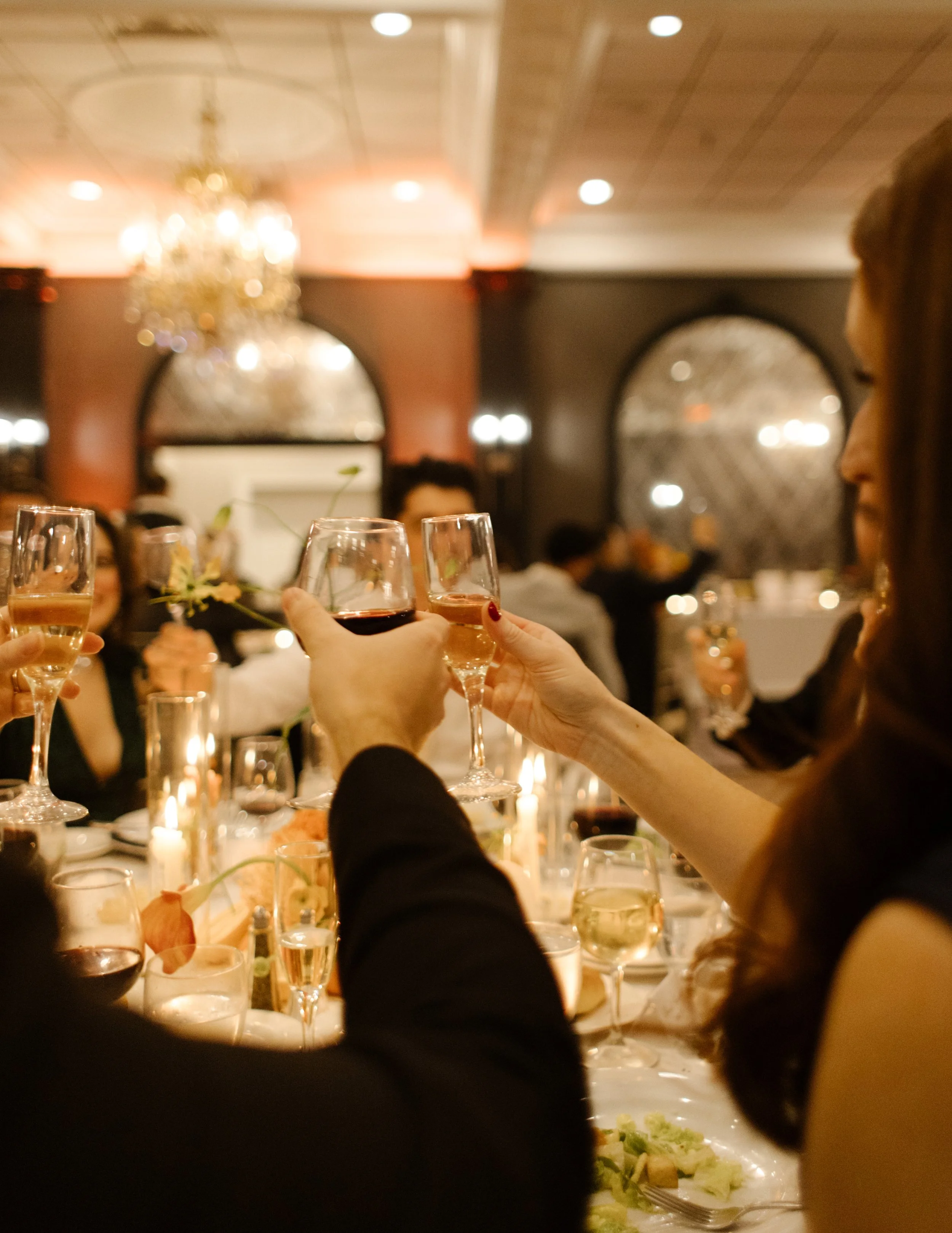 Guests raising glasses in a candlelit reception toast during an elegant evening wedding celebration
