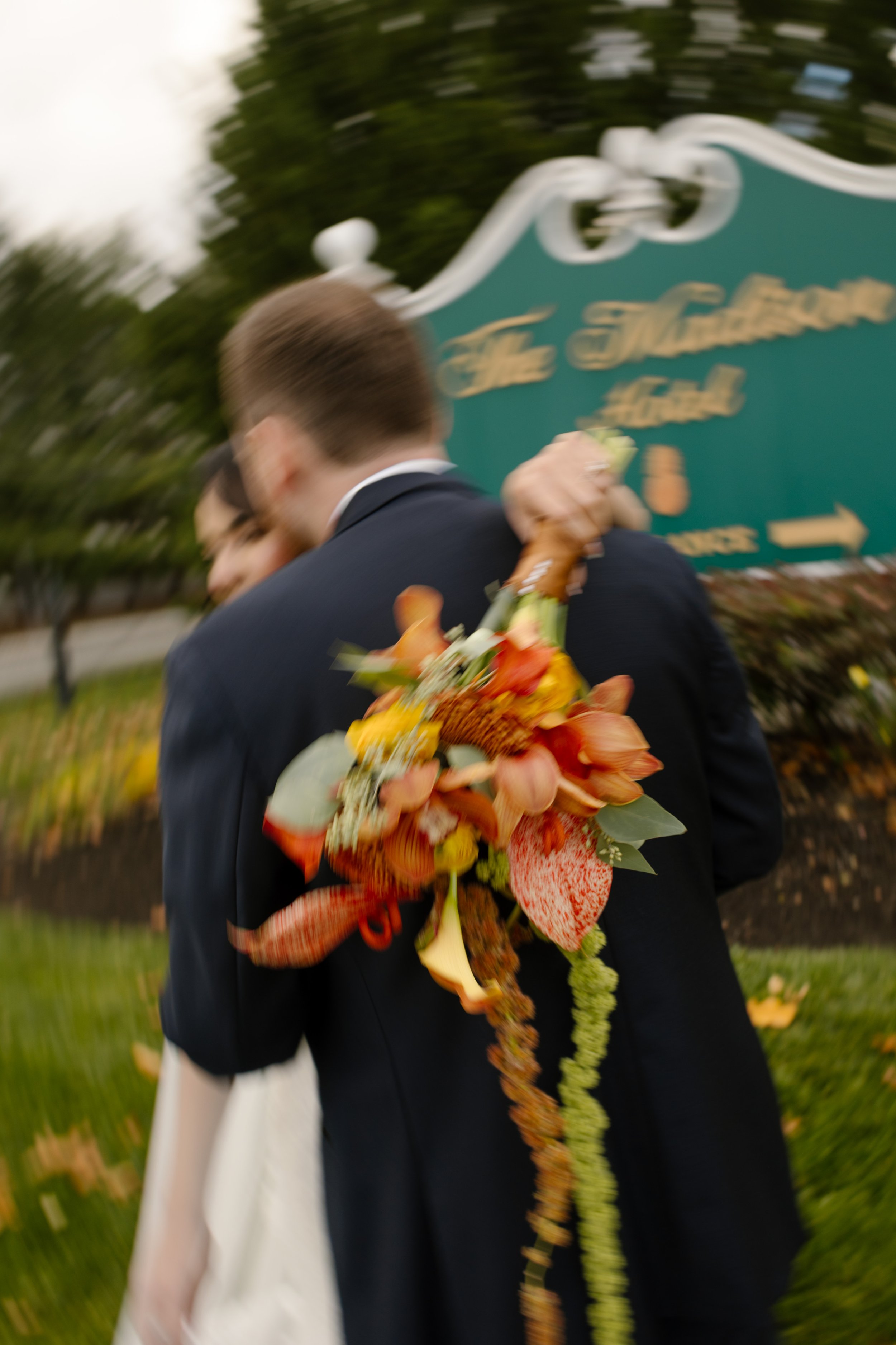 Newlyweds embracing outside the venue with a vibrant autumn wedding bouquet in motion