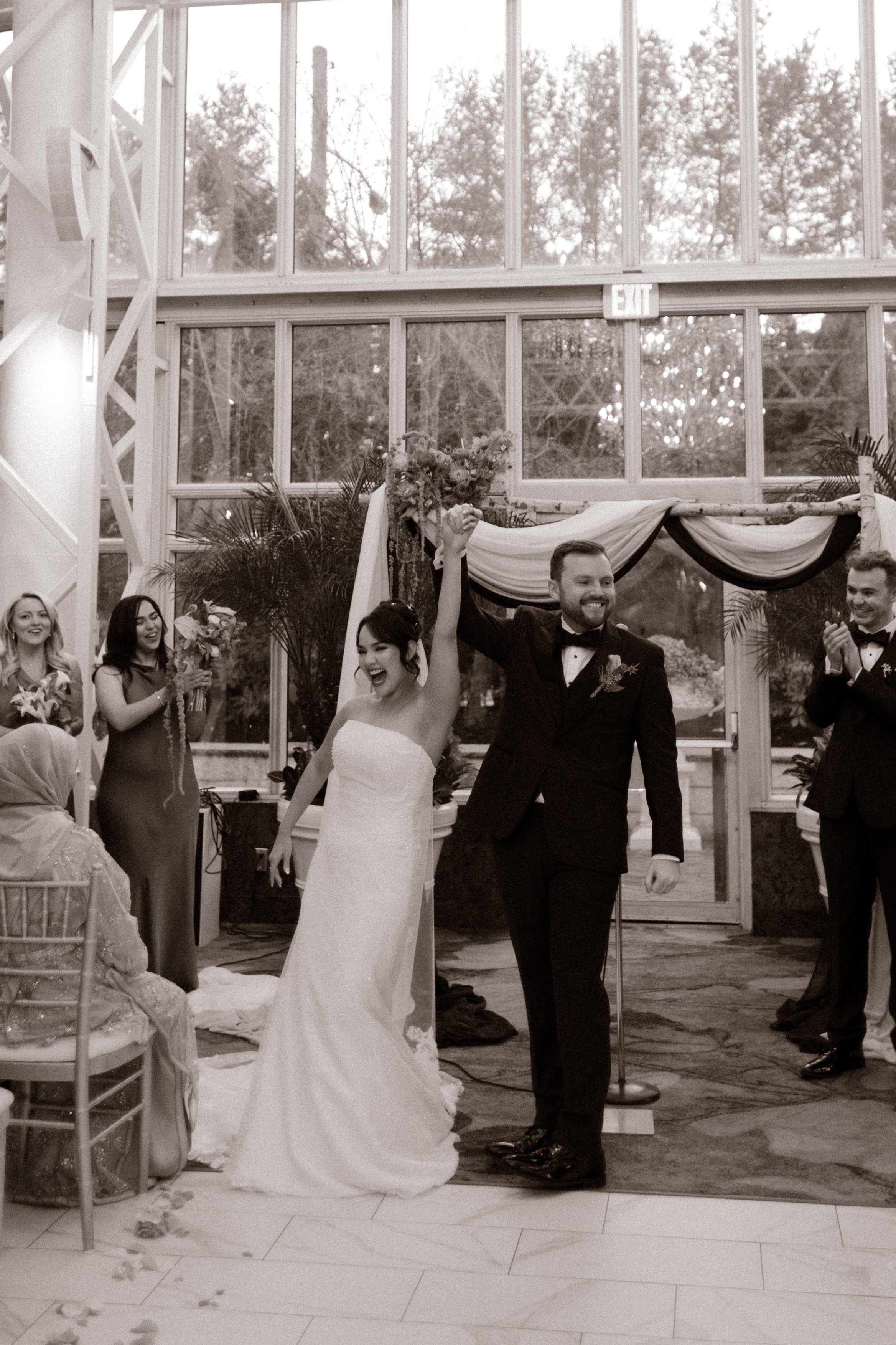 Newlyweds celebrating their ceremony exit in a glass conservatory during a joyful wedding in New York ceremony