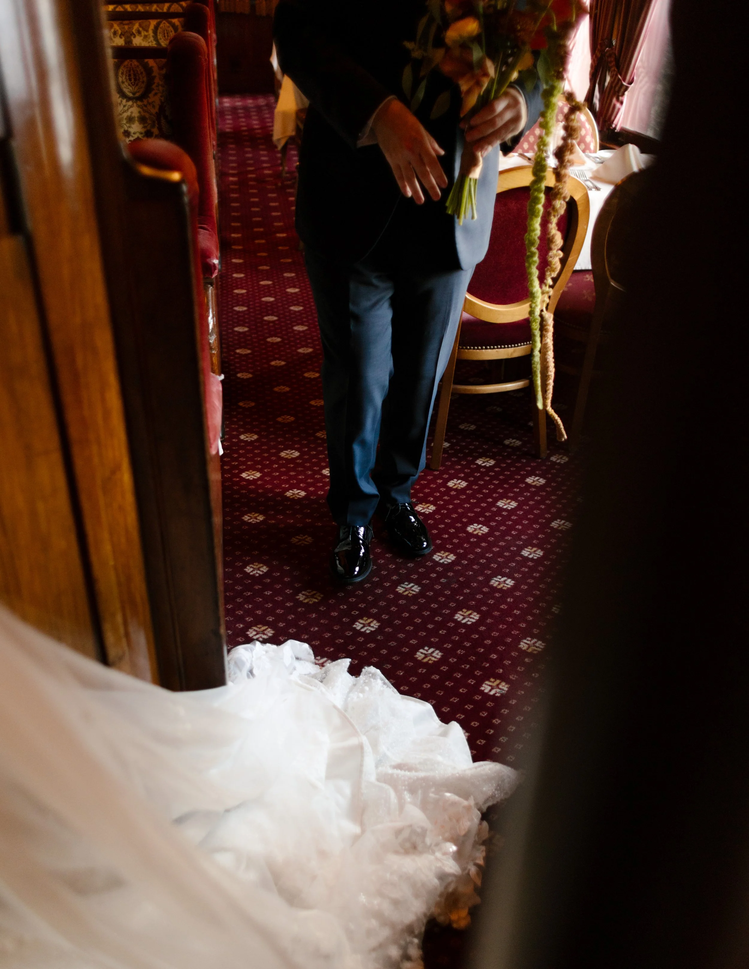 Groom holding a colorful wedding bouquet while waiting to see his bride inside a historic venue