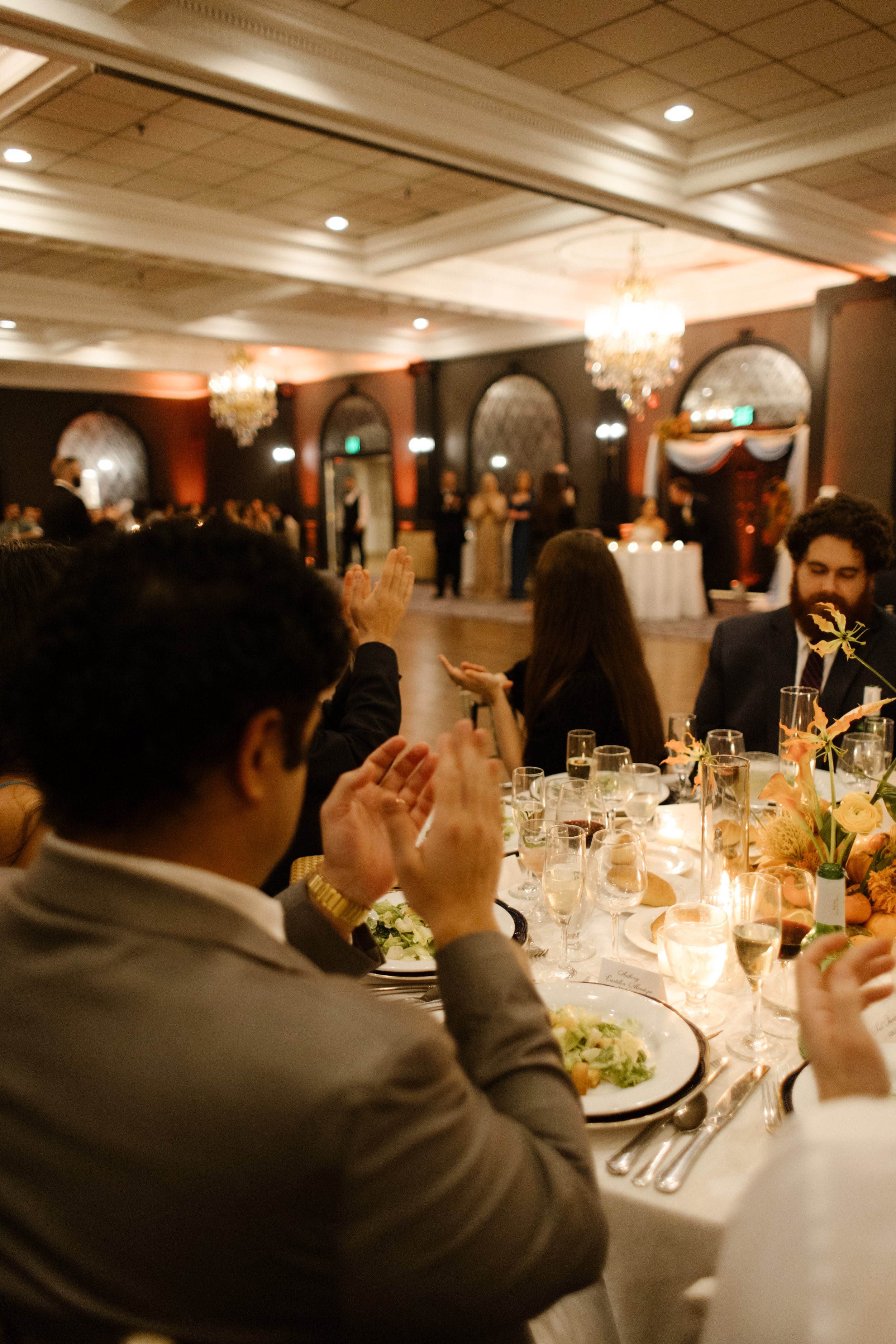 Wedding guests applauding during a reception speech at an elegant ballroom celebration